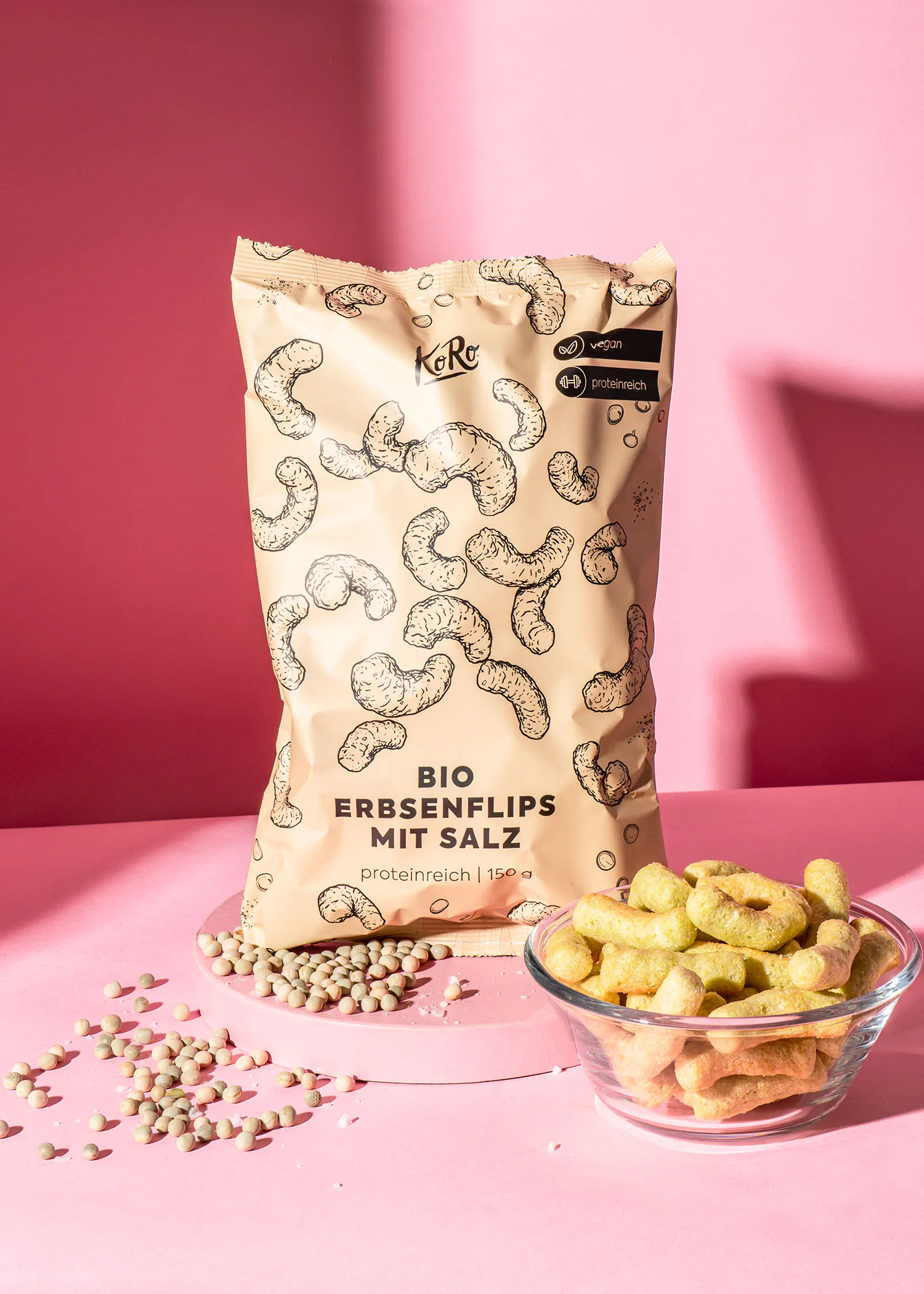un sac de chips bio erbsenflips mit salz est assis sur une table rose à côté d' un bol de chips