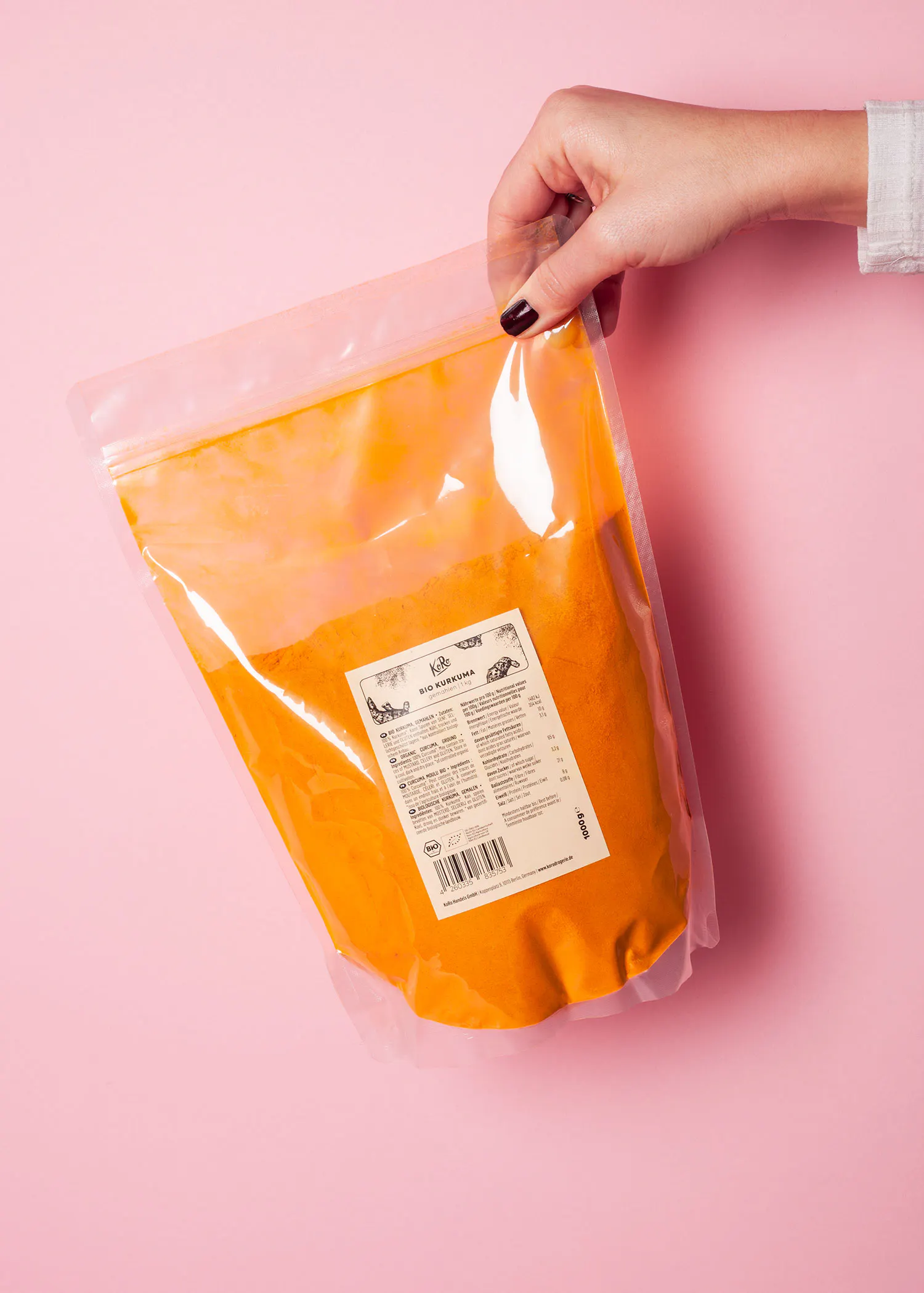a person is holding a bag of turmeric powder on a pink surface