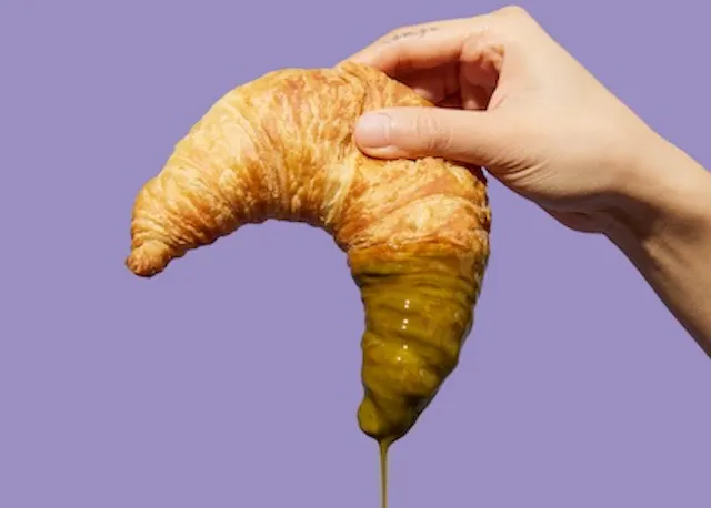 une personne tient un croissant avec une sauce verte coulant dessus