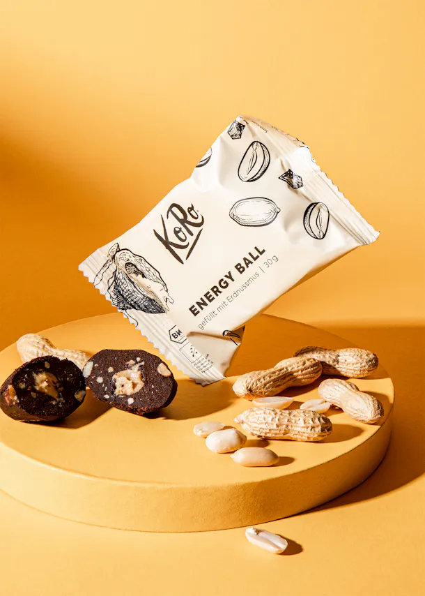 eine weiße verpackte energiekugel mit erdnussstücken