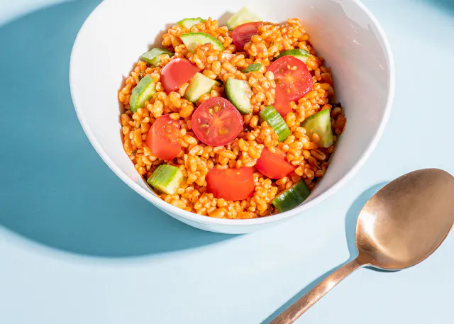 a bowl of food with tomatoes and cucumbers next to a gold spoon