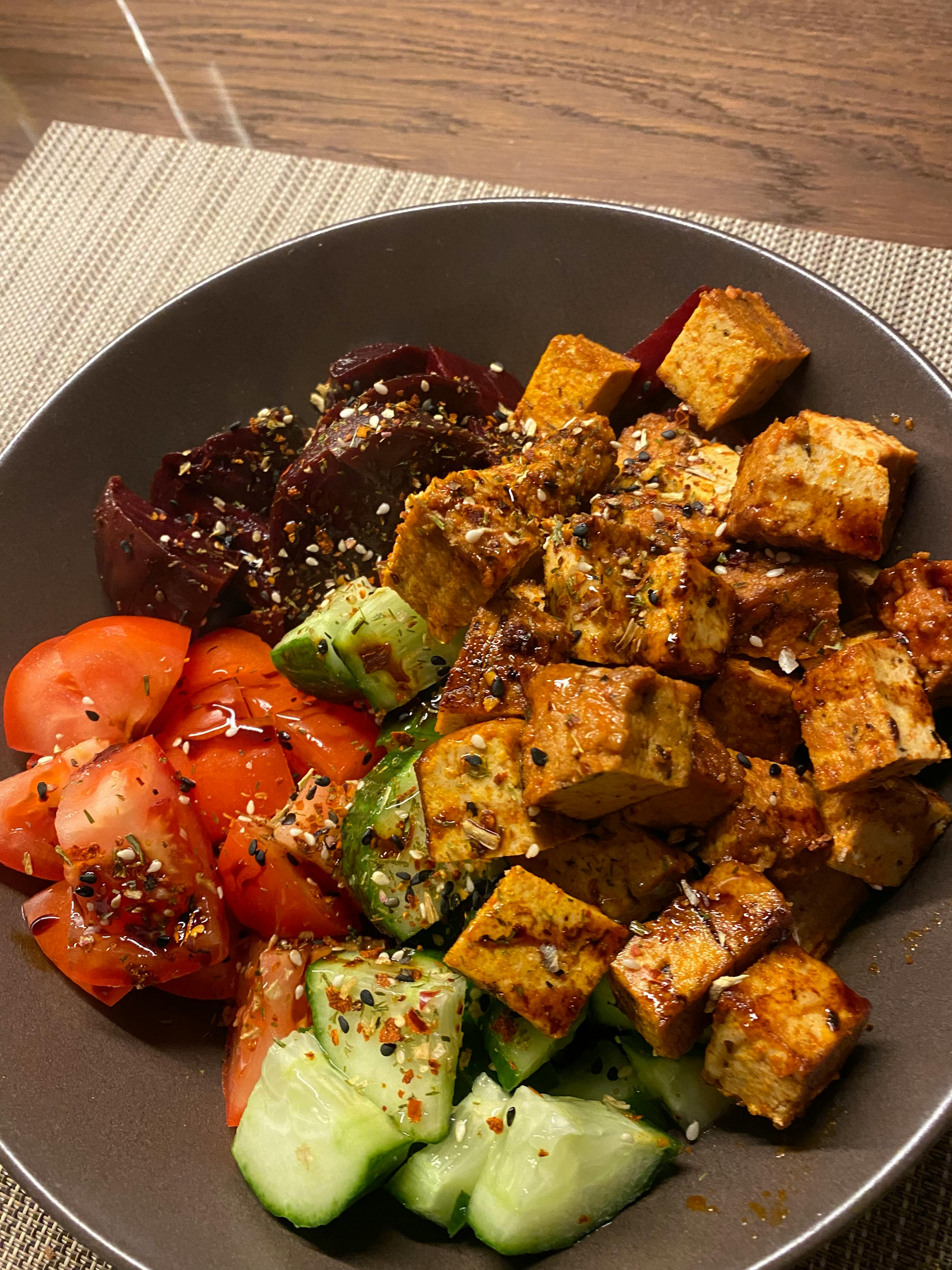 ein brauner Teller mit einem Salat und einem Stück Tofu darauf