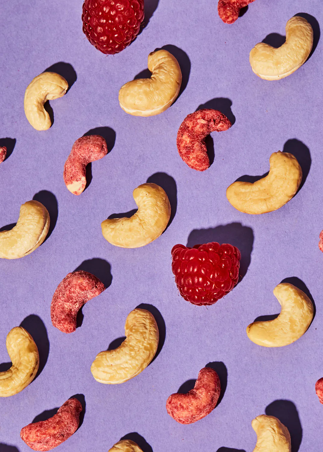 a pattern of cashews and raspberries on a purple surface