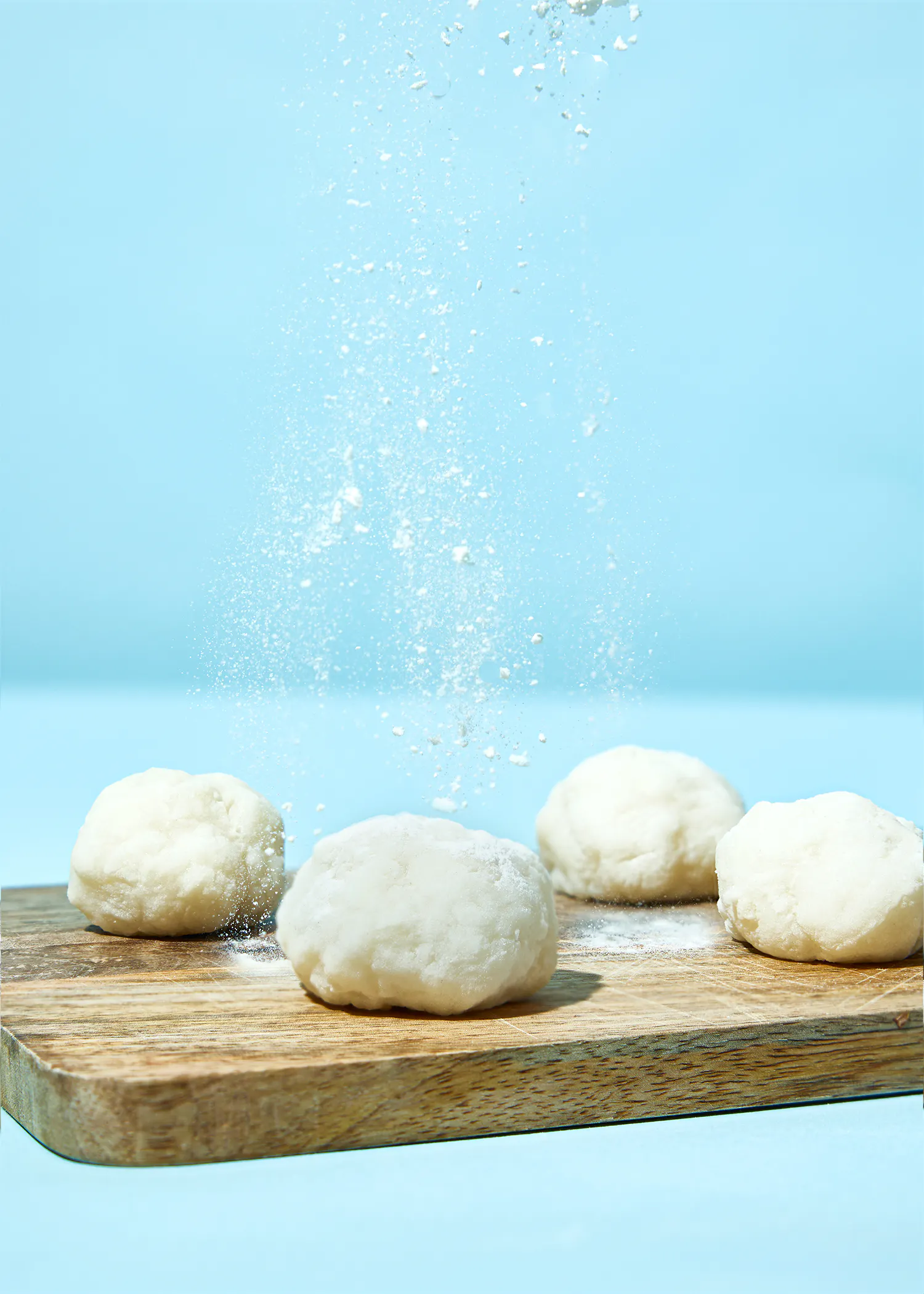four balls of dough on a cutting board with flour being sprinkled on them