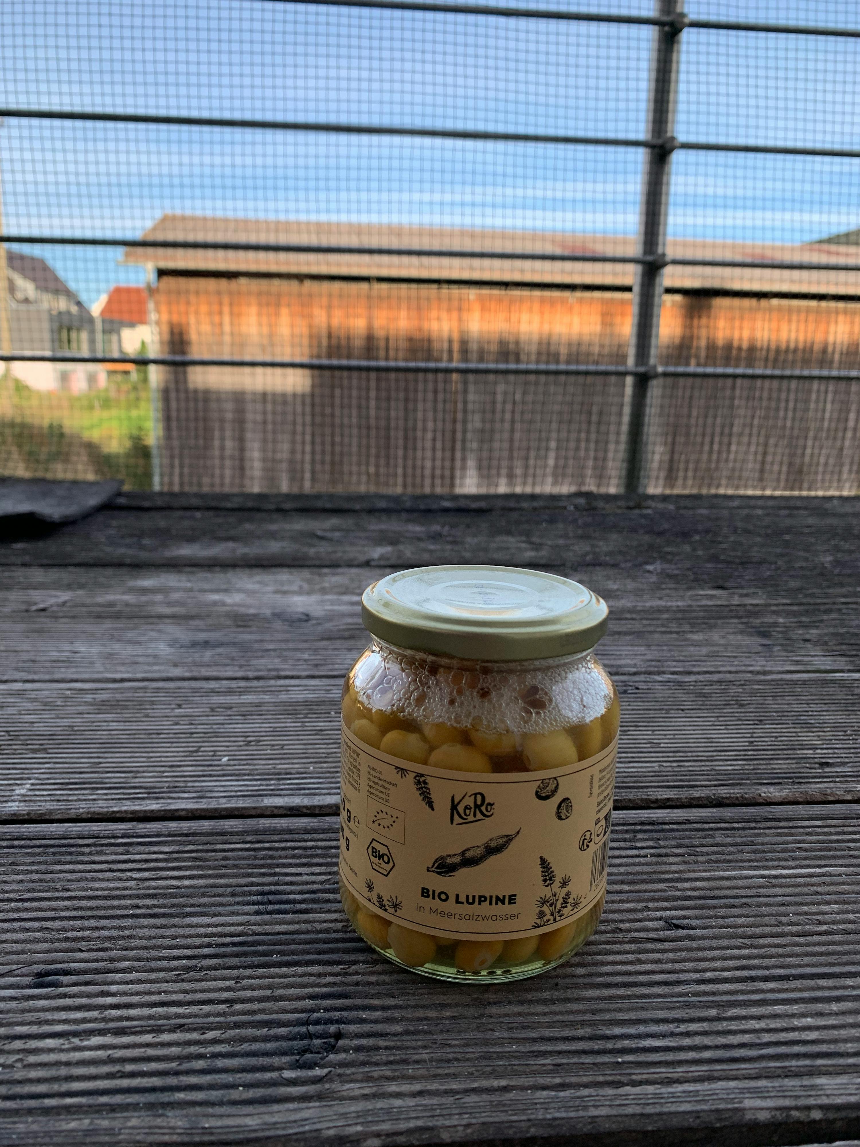 un bocal en verre rempli de haricots verts est posé sur une table en bois