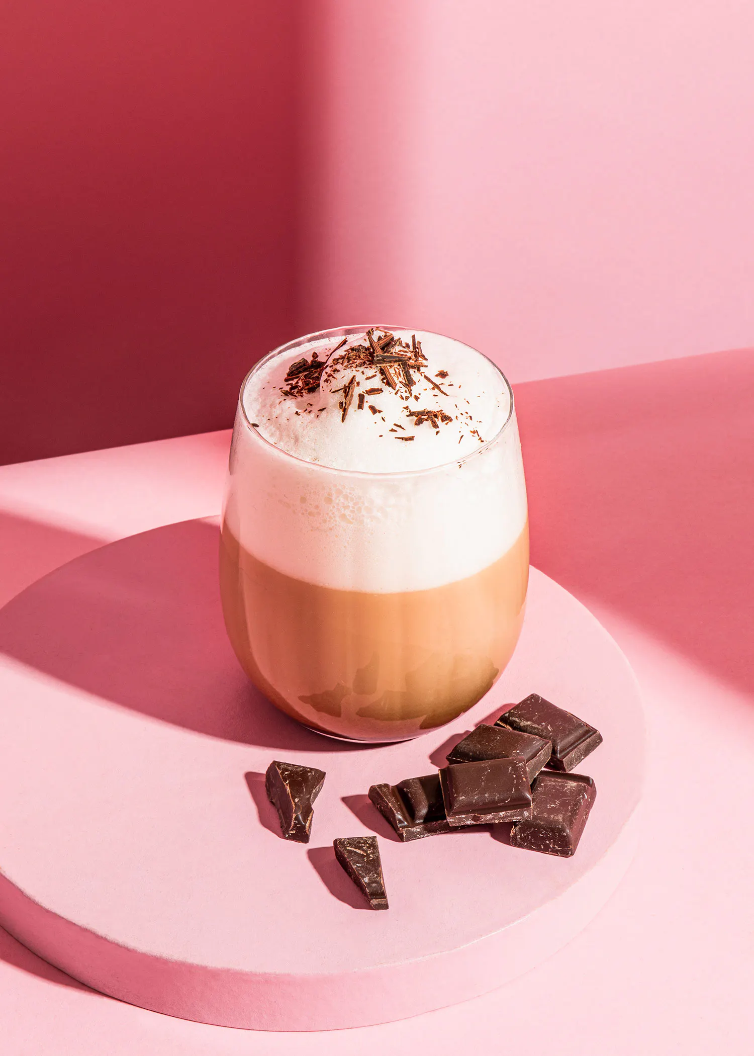 un verre de cappuccino avec des morceaux de chocolat sur une table rose