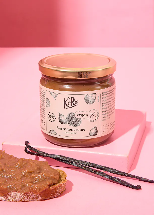 ein Glas maronencreme steht auf einem rosa Tisch neben einem Stück Brot