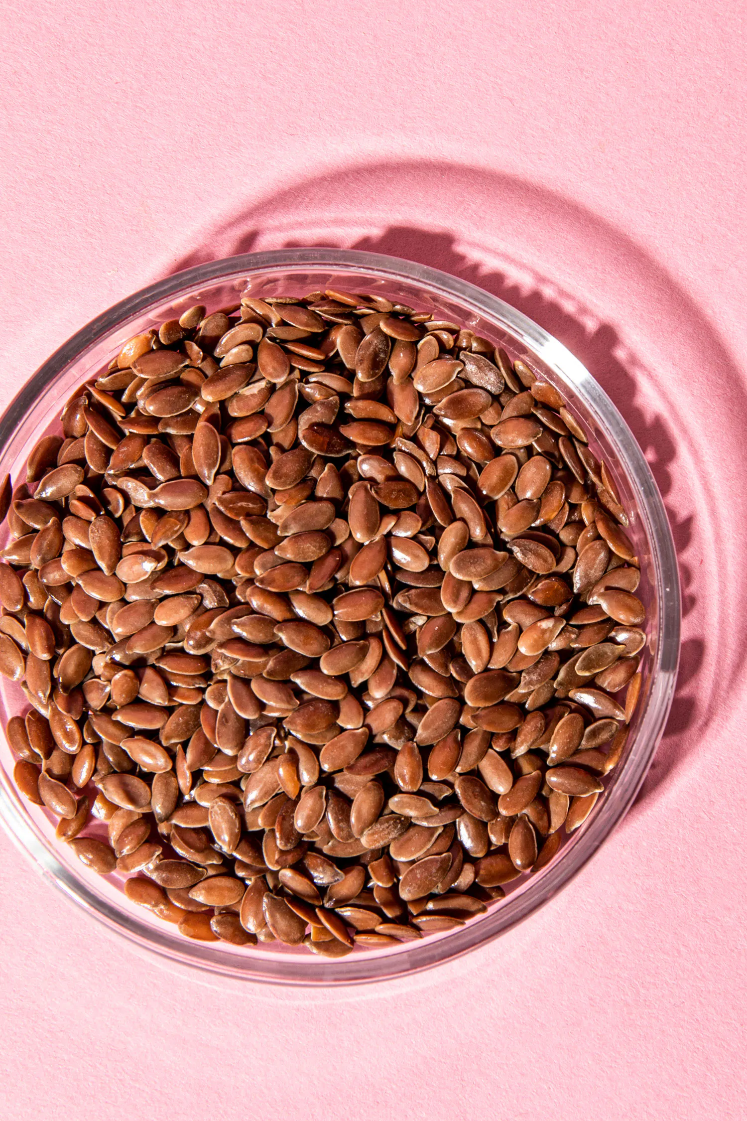 un bol en verre rempli de graines de lin sur un fond rose