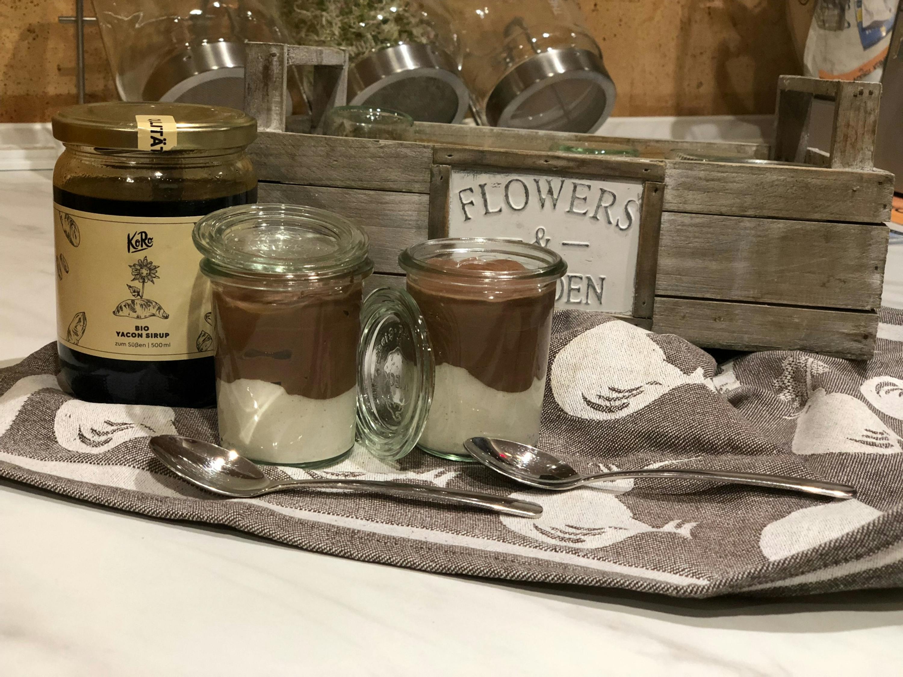 deux pots de dessert sont posés sur une table à côté d' une boîte de fleurs