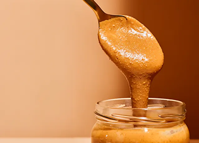 Erdnussbutter wird mit einem Löffel in ein Glas gegossen