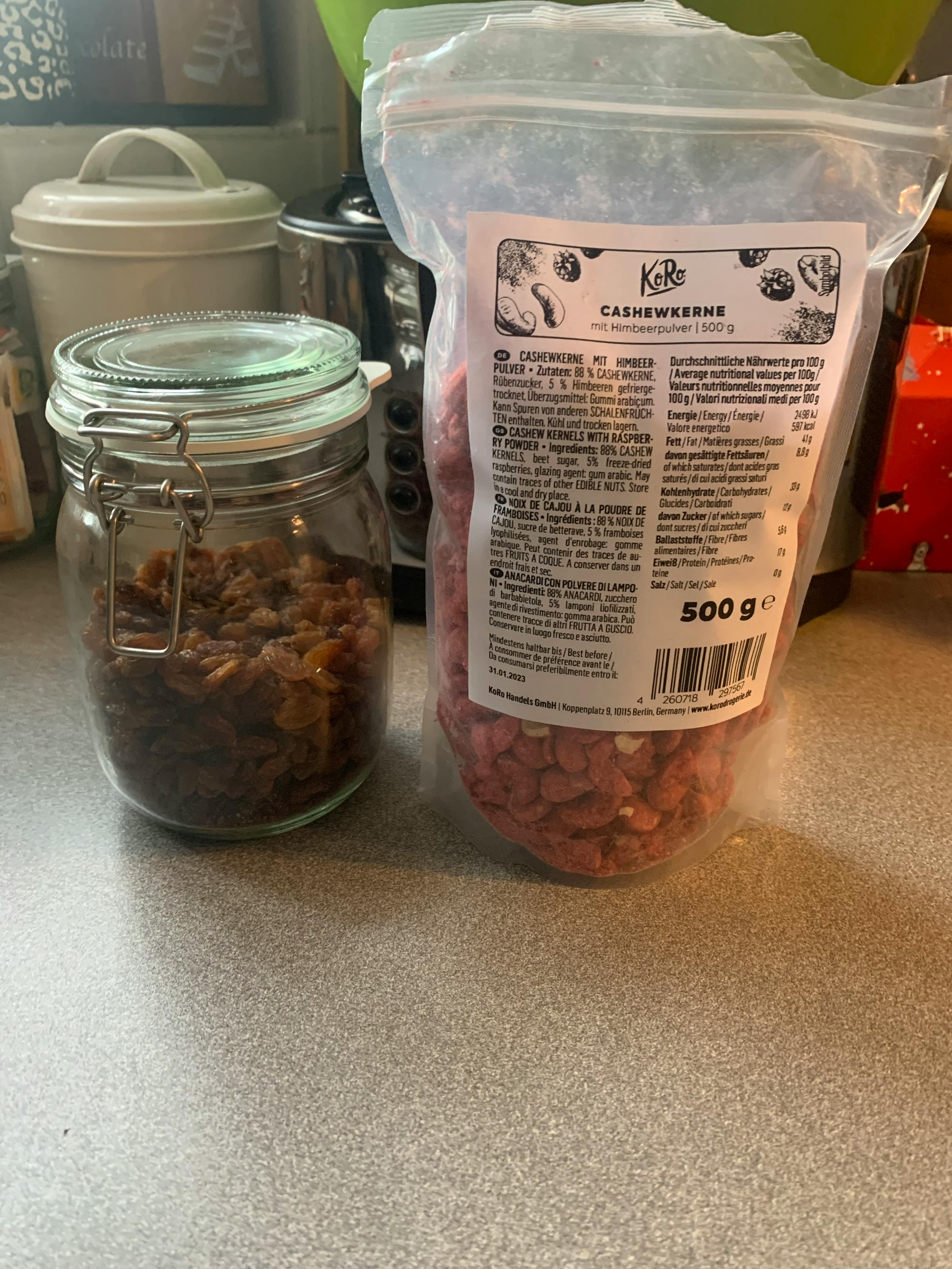 ein Glas mit getrockneten Rosinen neben einem Plastikbeutel mit Erdnüssen