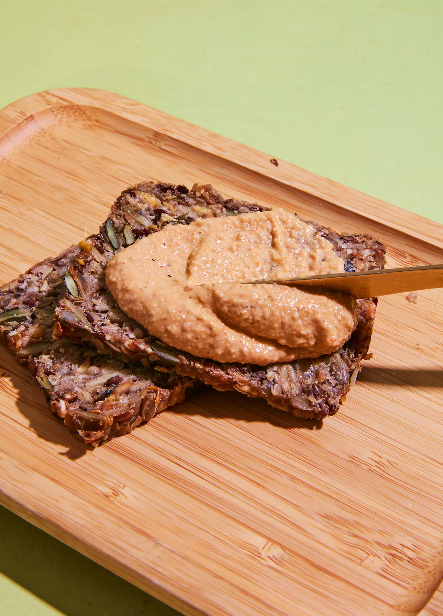 Auf einem Schneidebrett wird Erdnussbutter auf ein Stück Brot gestrichen