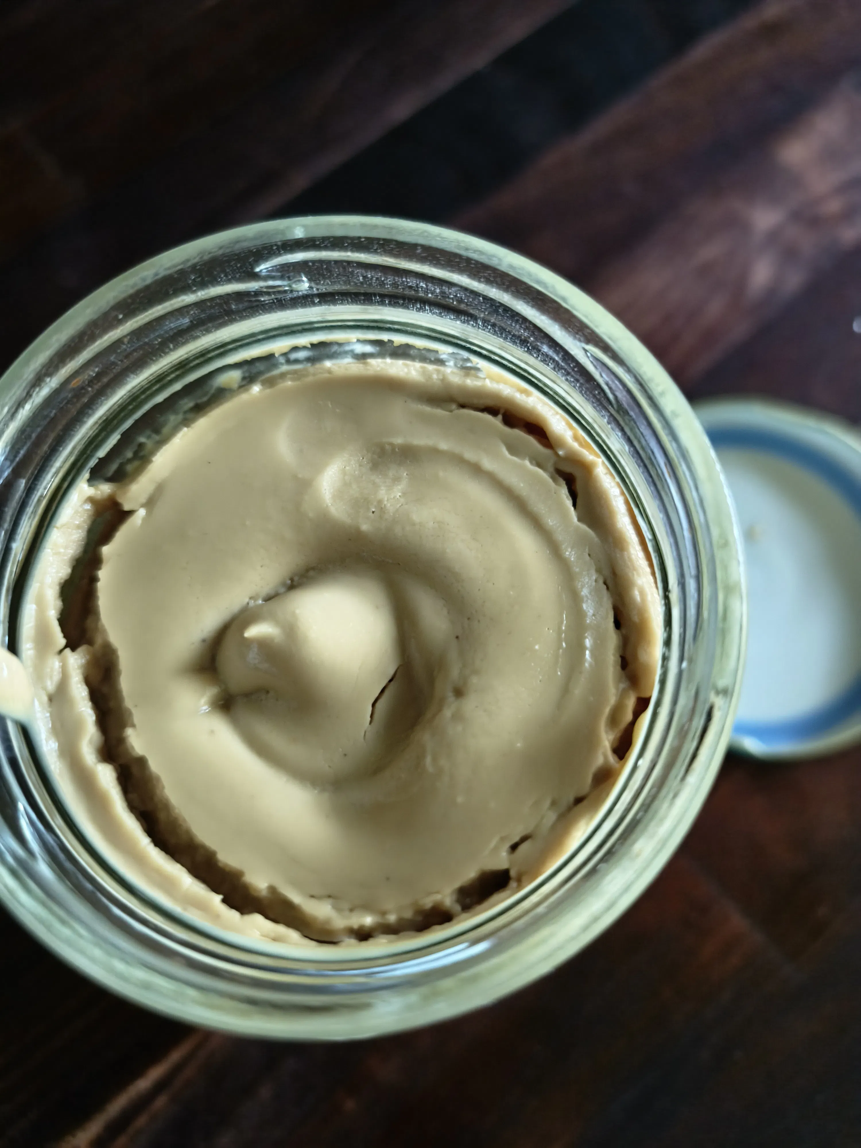 un vasetto aperto di crema spalmabile beige chiaro e liscia con una superficie ondulata.