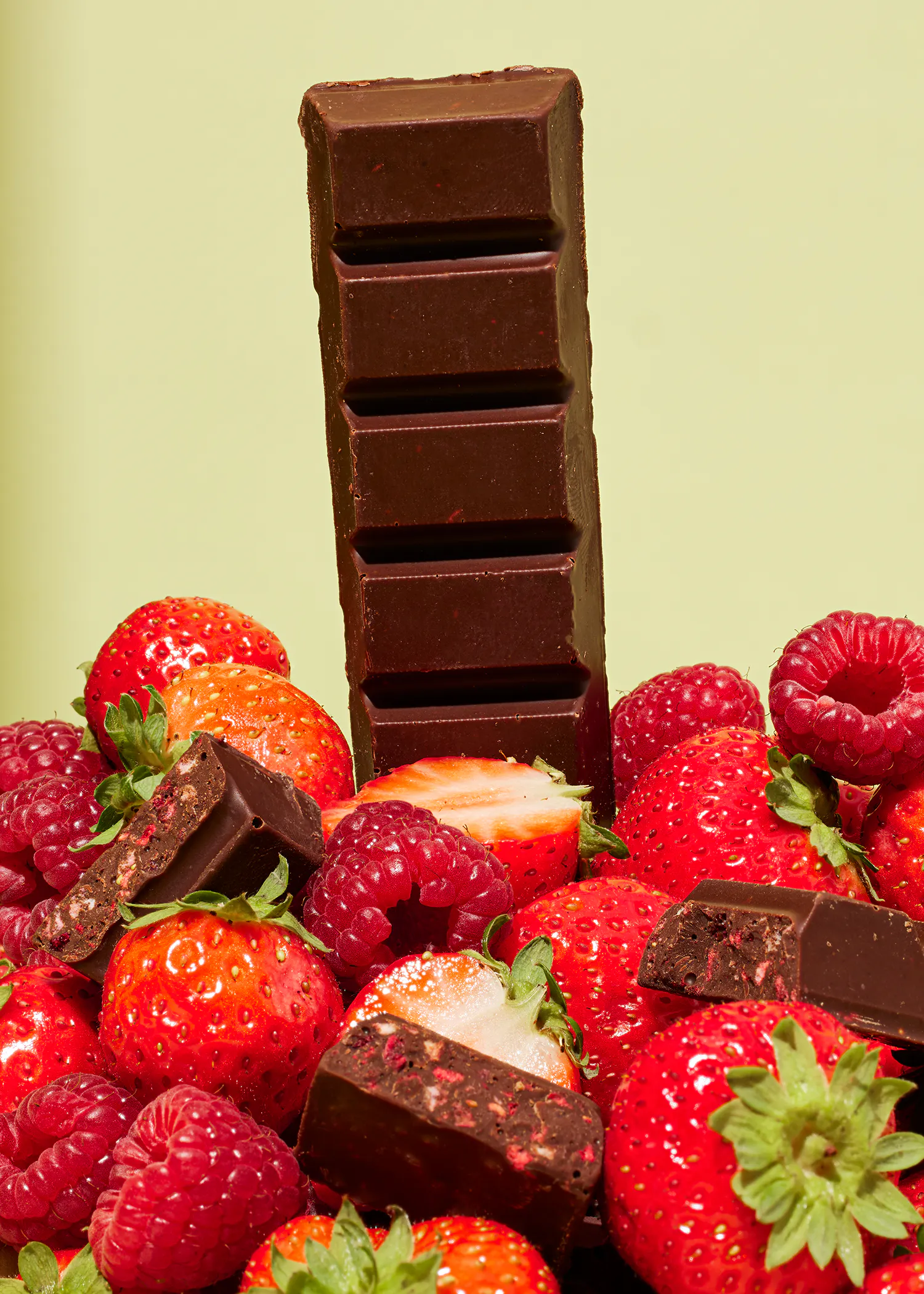 une barre de chocolat est posée sur une pile de fraises et de framboises