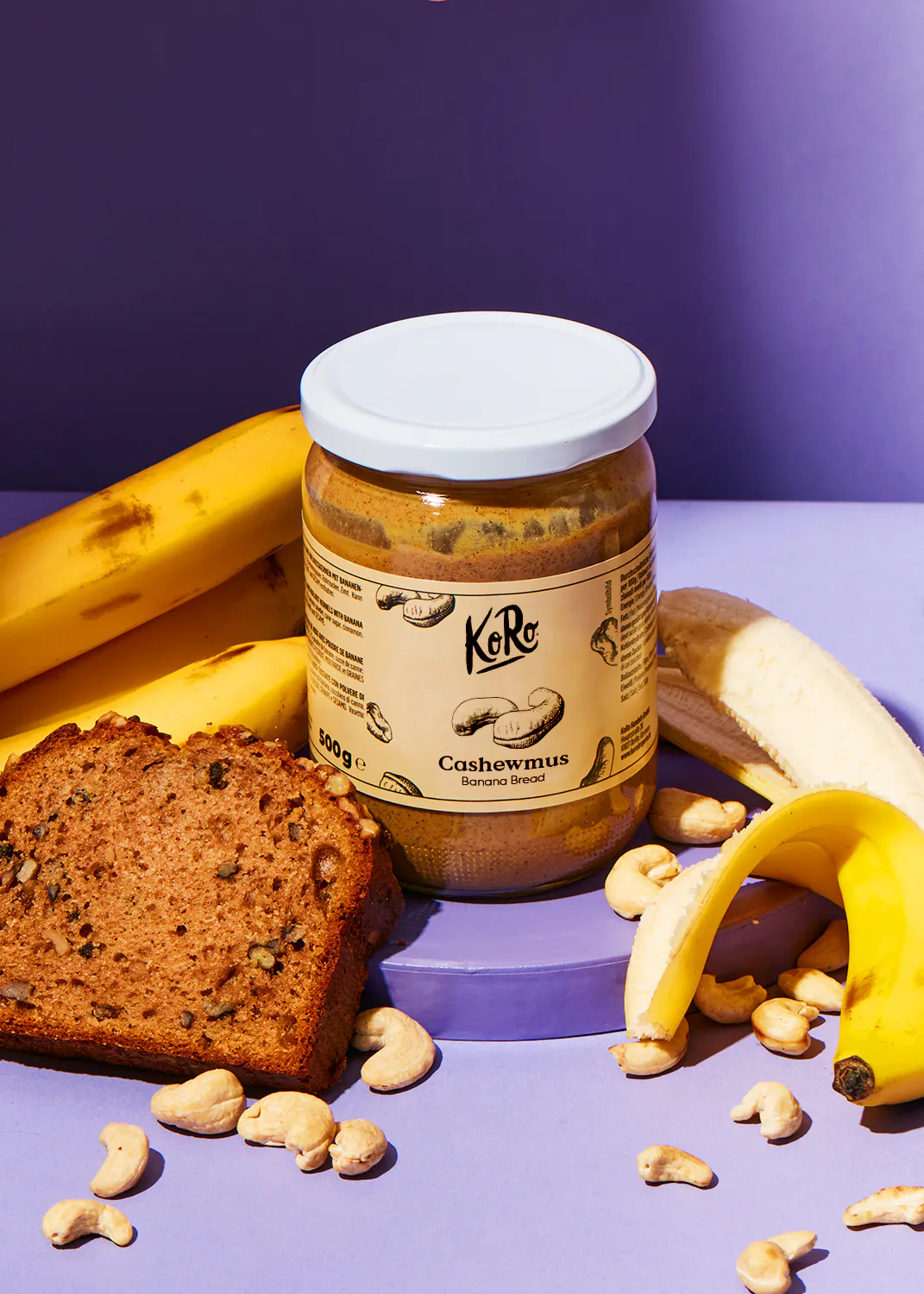 ein Glas Cashewmus neben einem Bananenbrot und Bananen