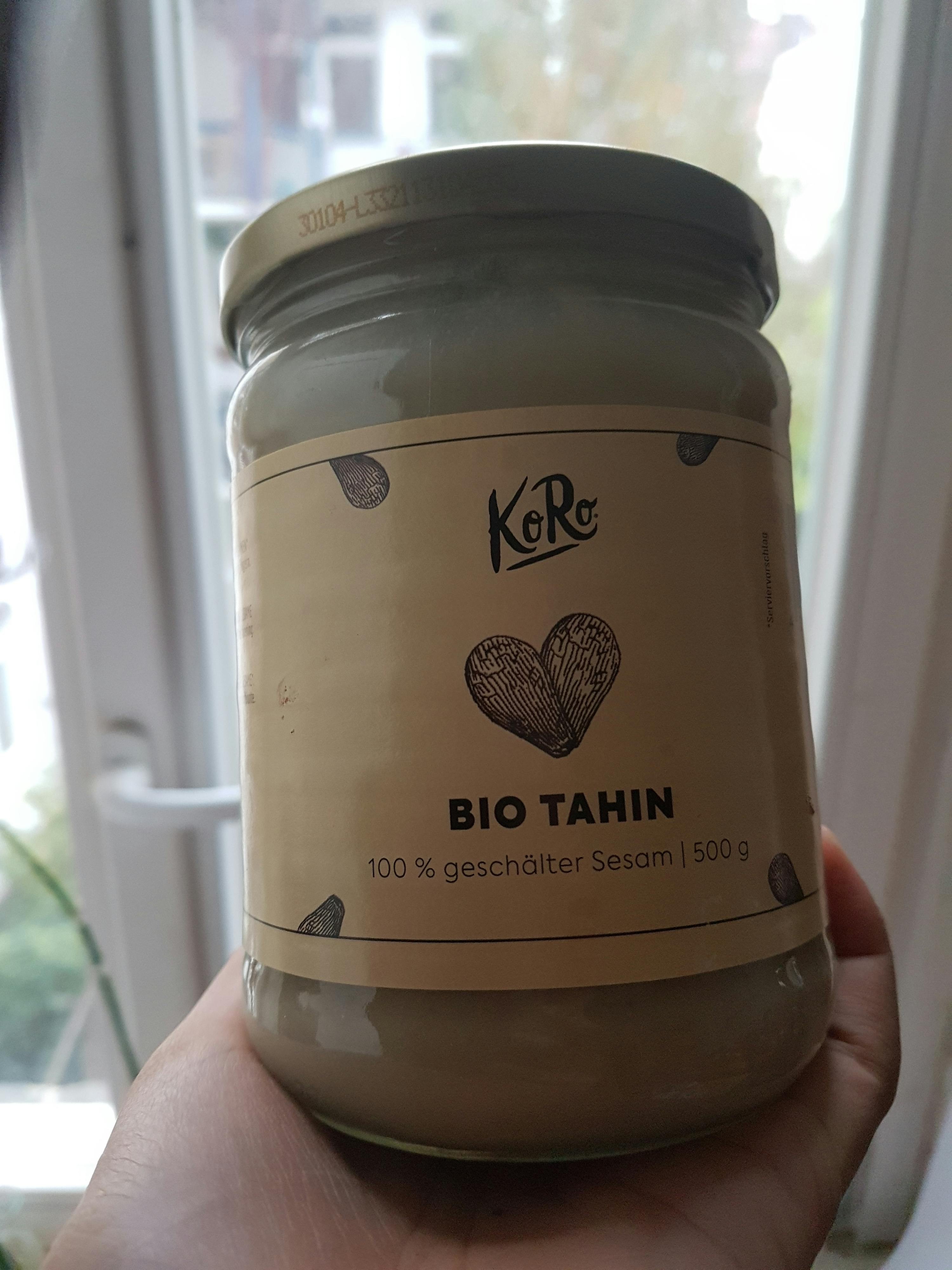 eine Person hält ein Glas bio Tahin vor einem Fenster
