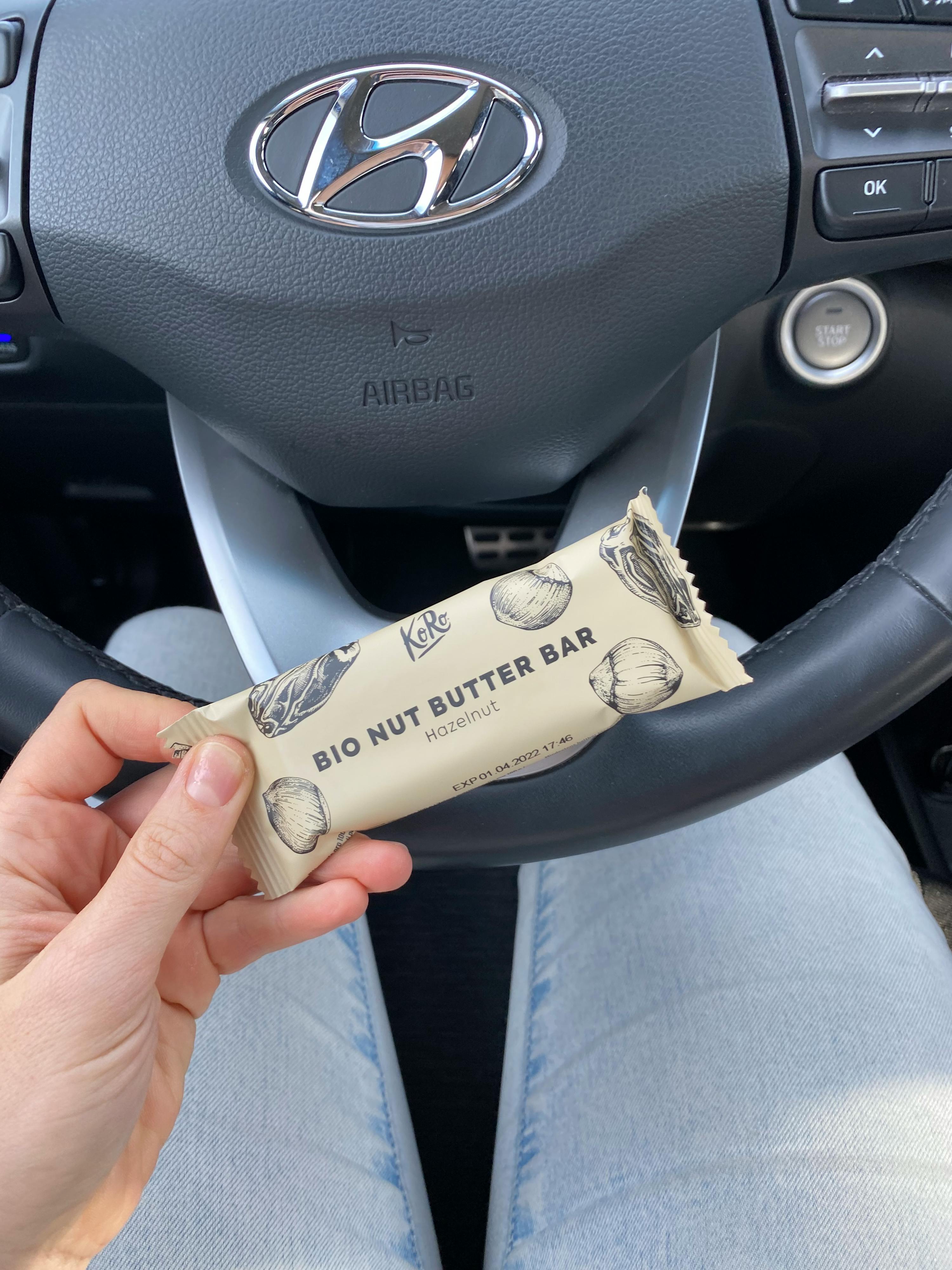 a person holding a bio nut butter bar in front of a steering wheel