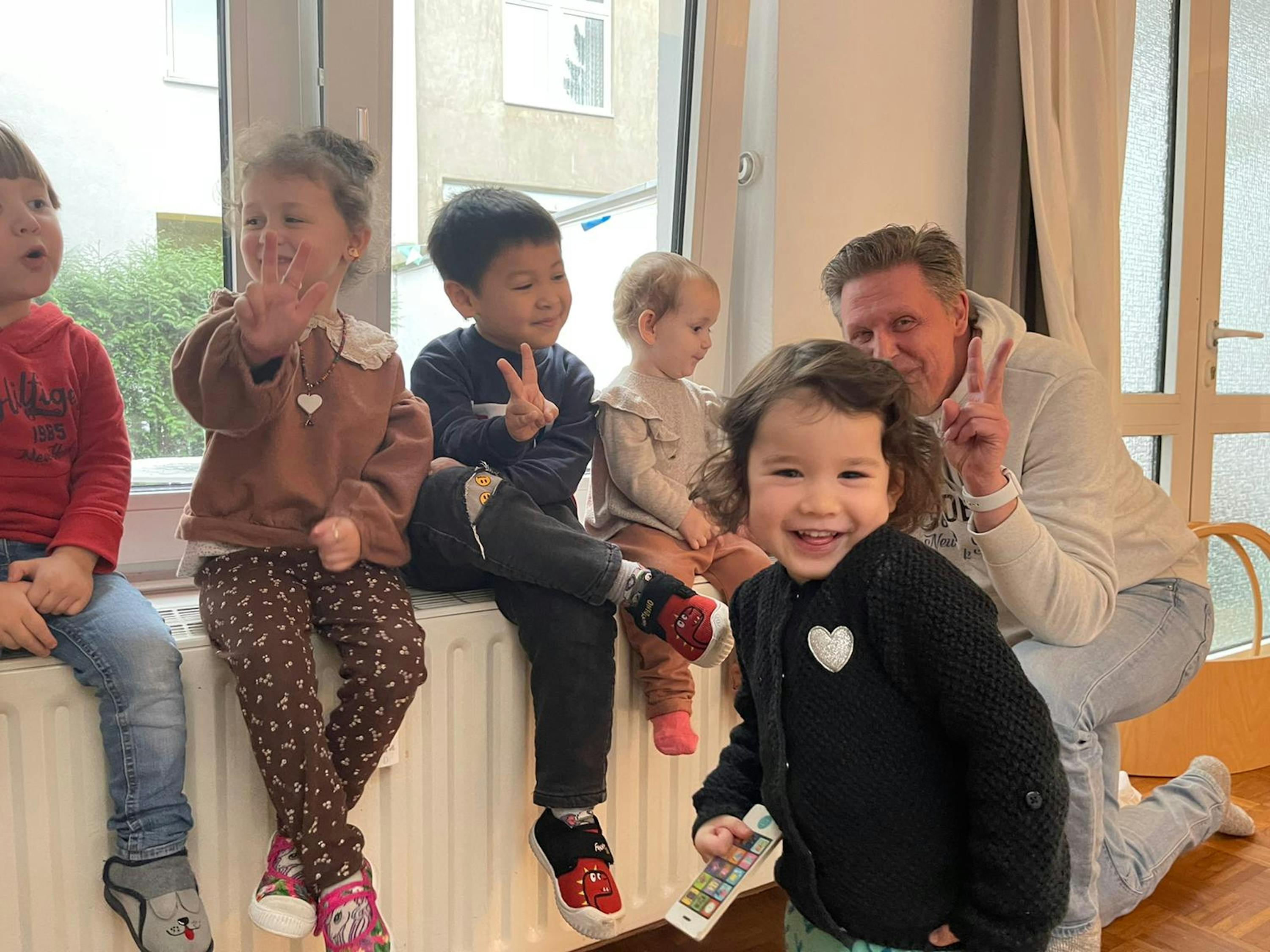 un groupe d' enfants sont assis sur un radiateur et un homme donne un signe de la paix
