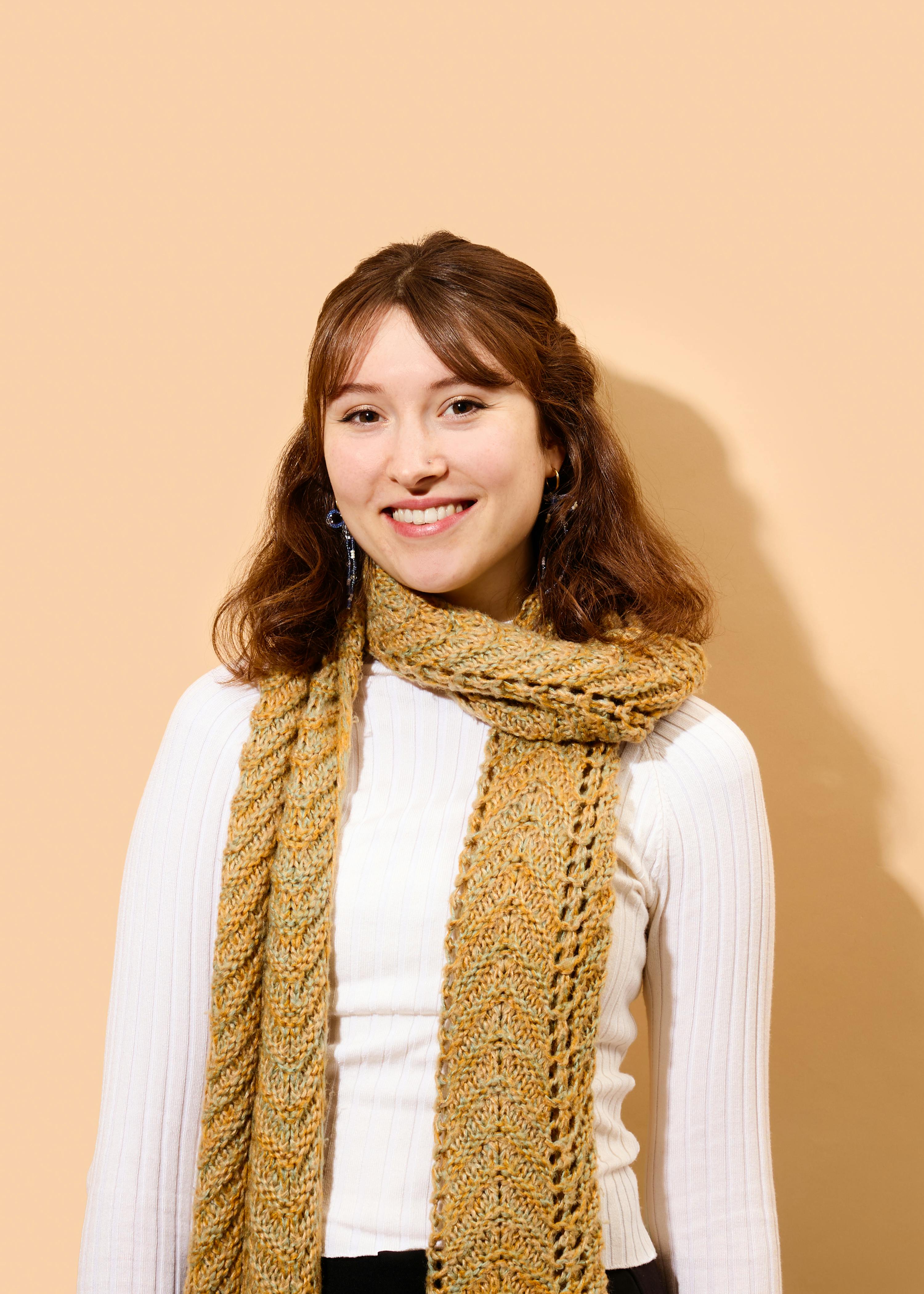 Eine Frau trägt einen weißen Pullover und einen gelben Schal und lächelt