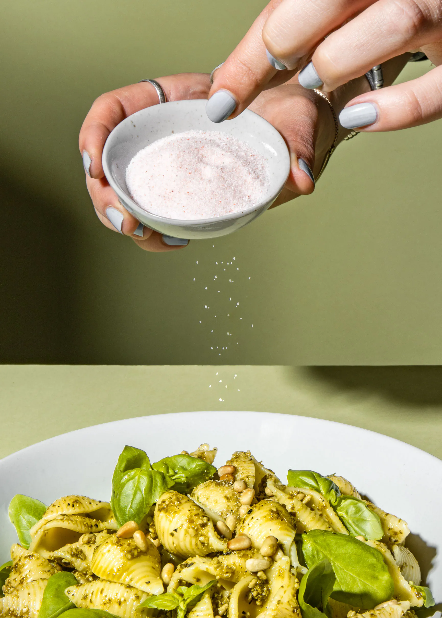une personne secoue du sel sur une assiette de pâtes