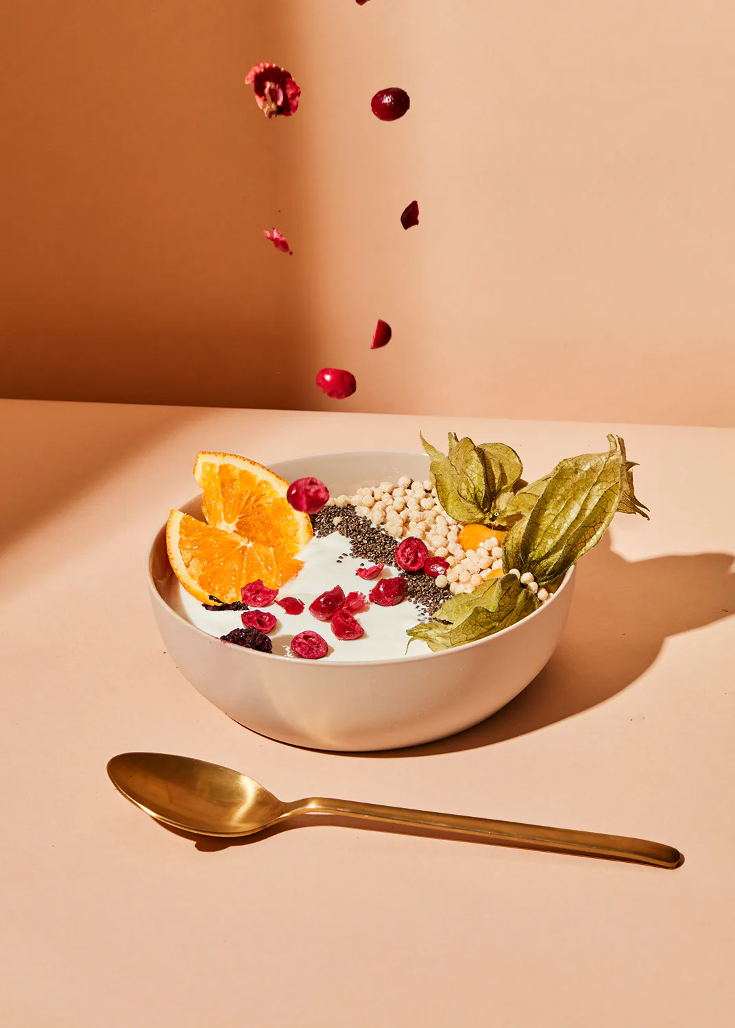 a bowl of yogurt with berries and oranges and a gold spoon