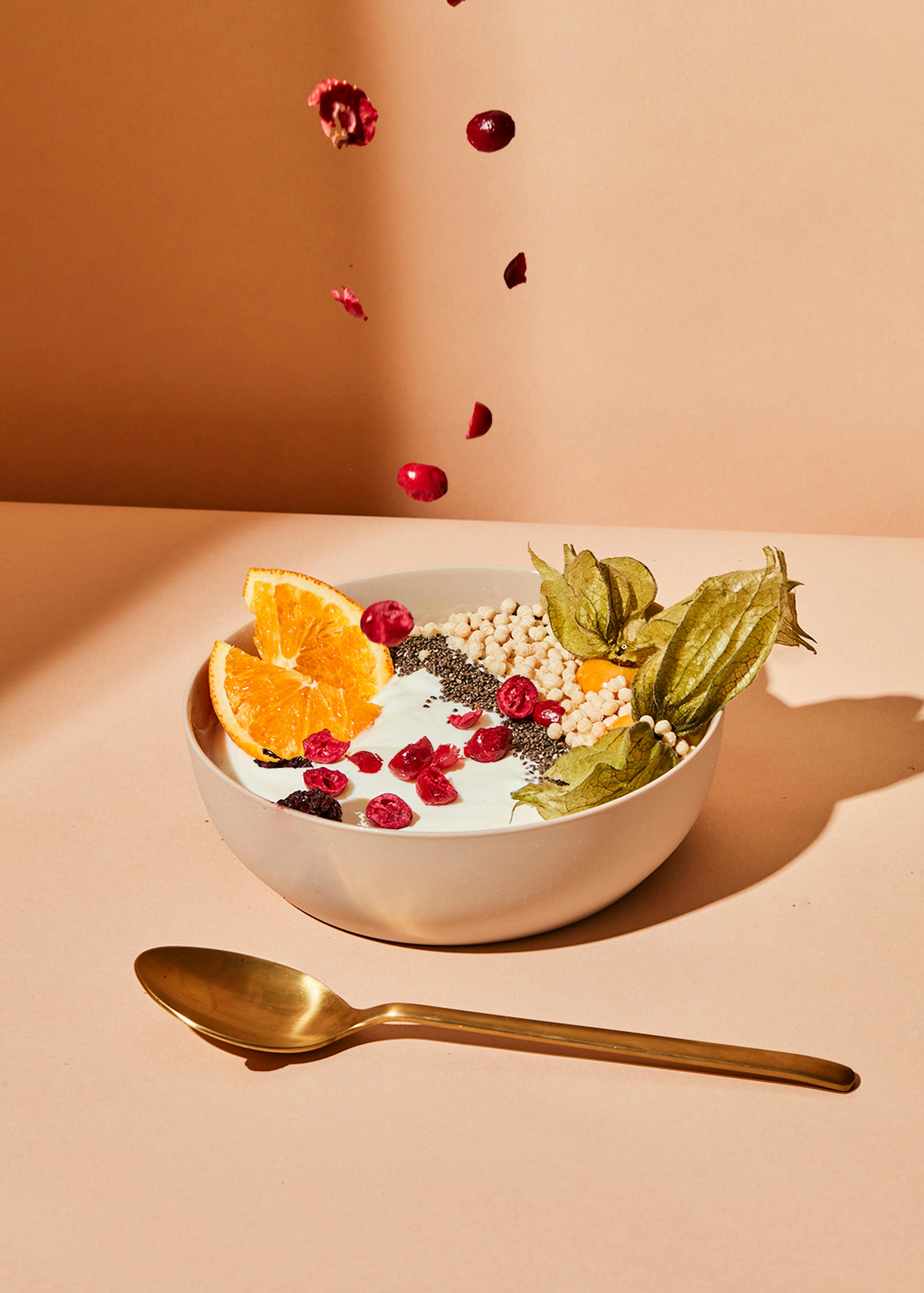 a bowl of yogurt with berries and oranges and a gold spoon
