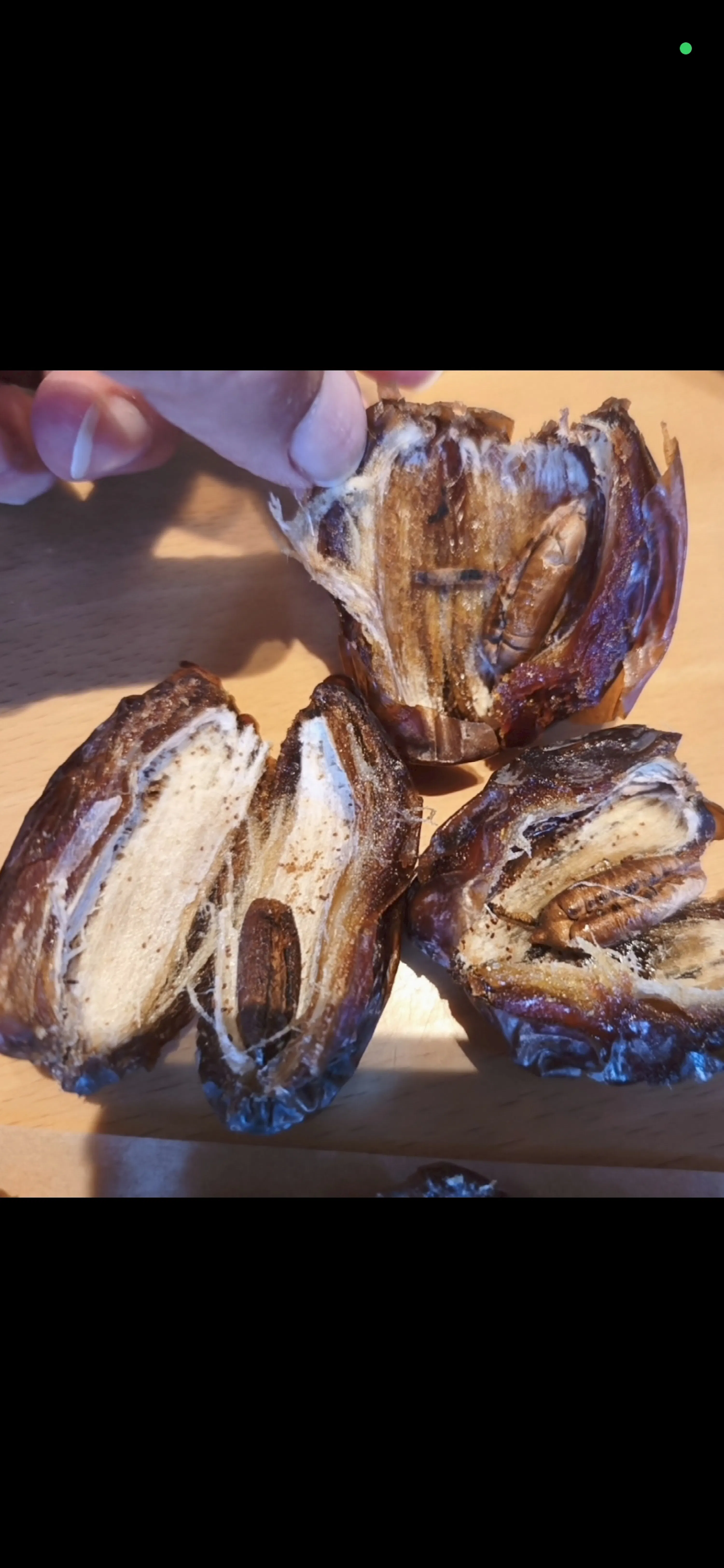 a hand holds open a date, revealing its seed and fibrous interior, with two other split dates resting on a wooden surface.