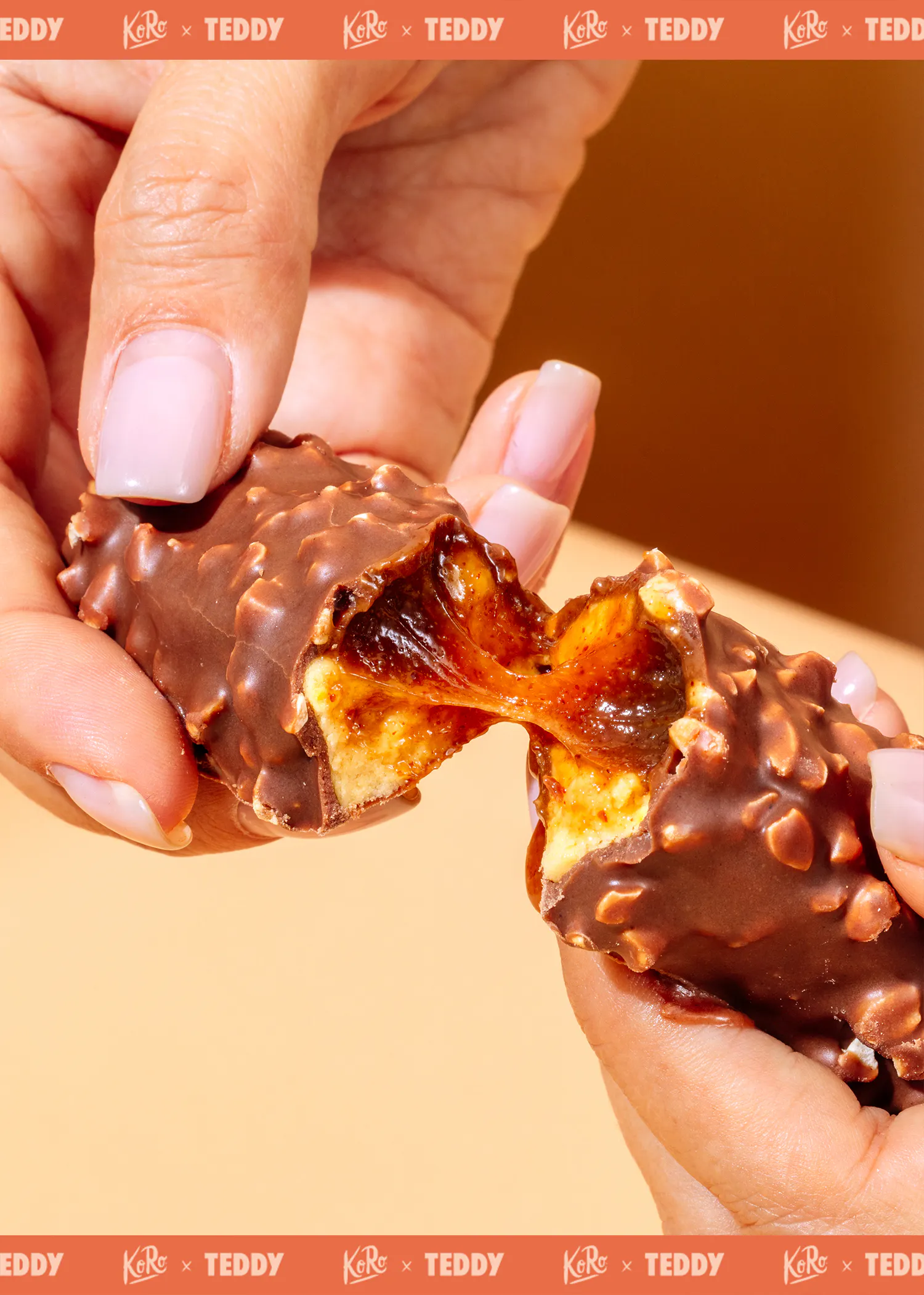 deux mains séparent une barre chocolatée croustillante aux éclats de noix, révélant un cœur de caramel filant et de nougat.