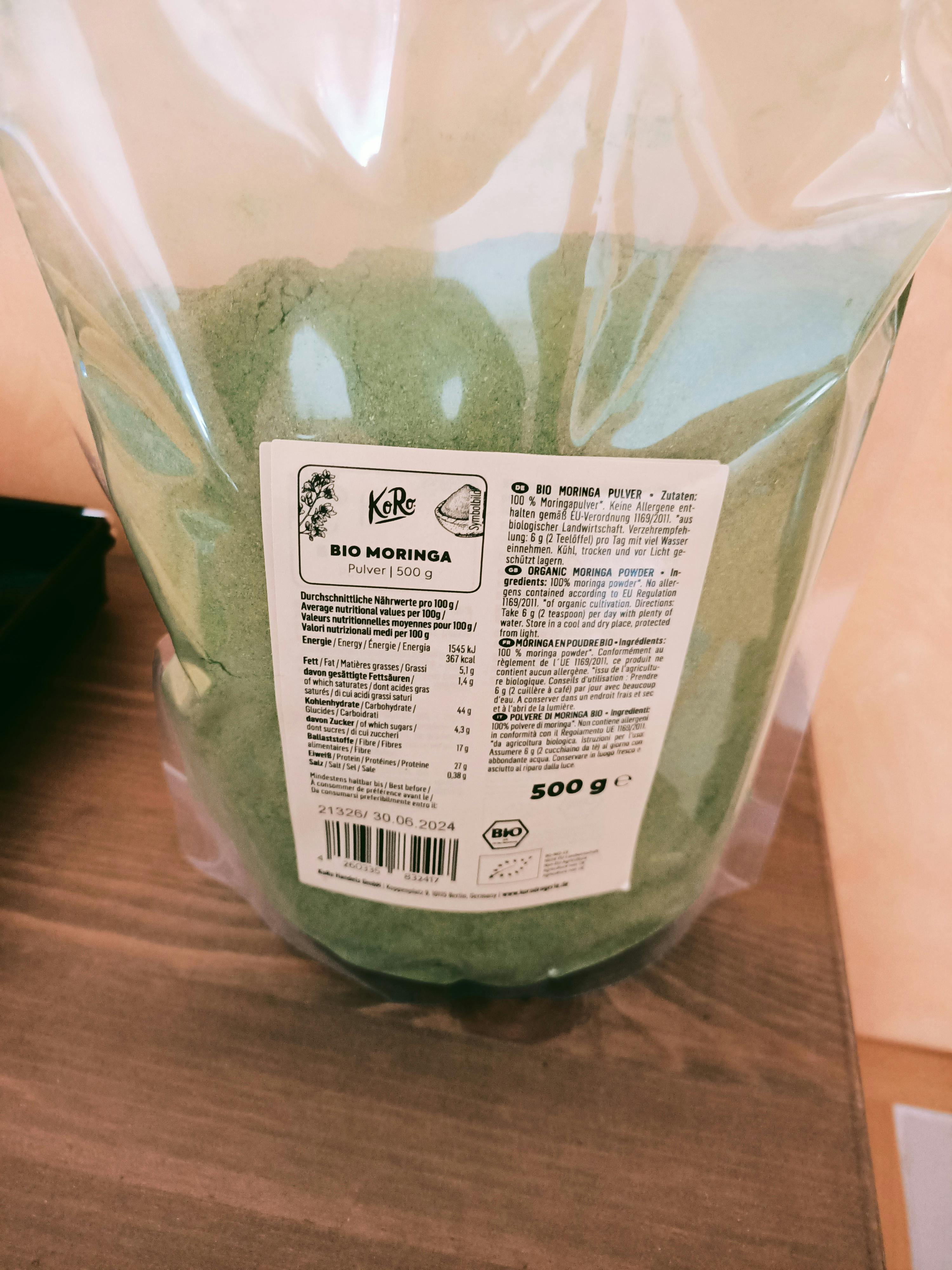 un sac de poudre de moringa bio est assis sur une table en bois