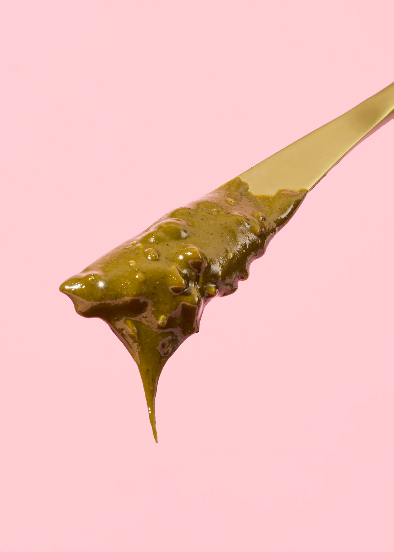 ein goldener Löffel mit grüner Soße auf einem rosa Hintergrund