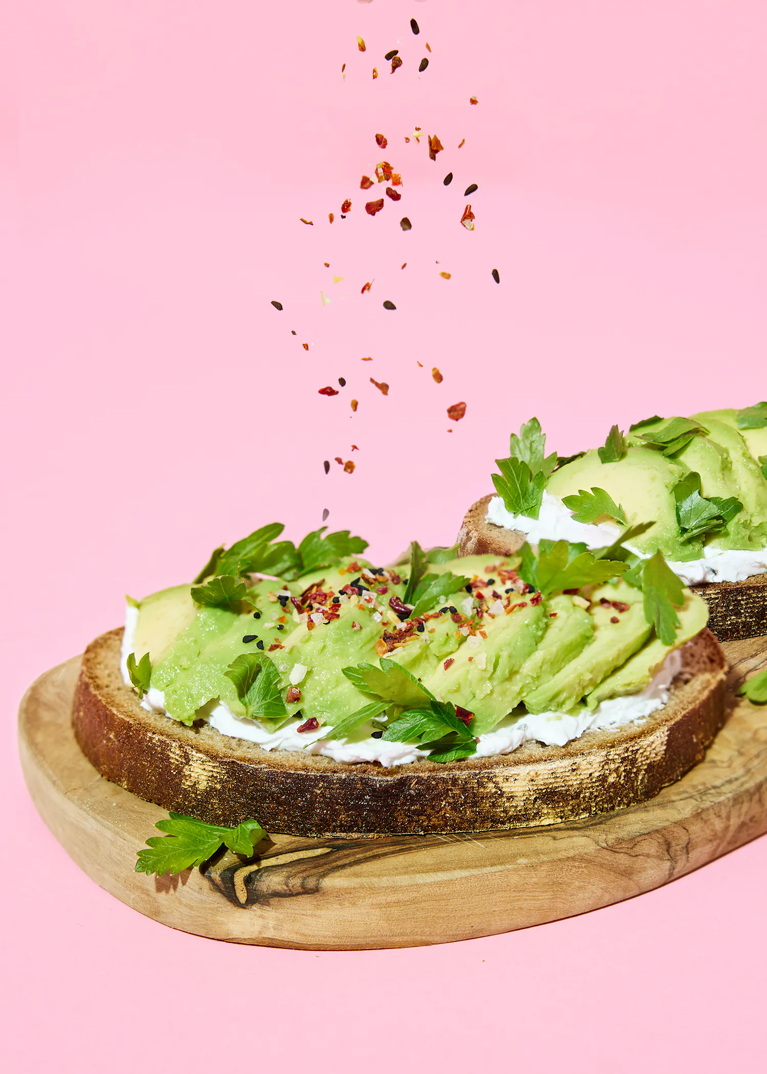 two slices of avocado toast on a wooden cutting board on a pink background