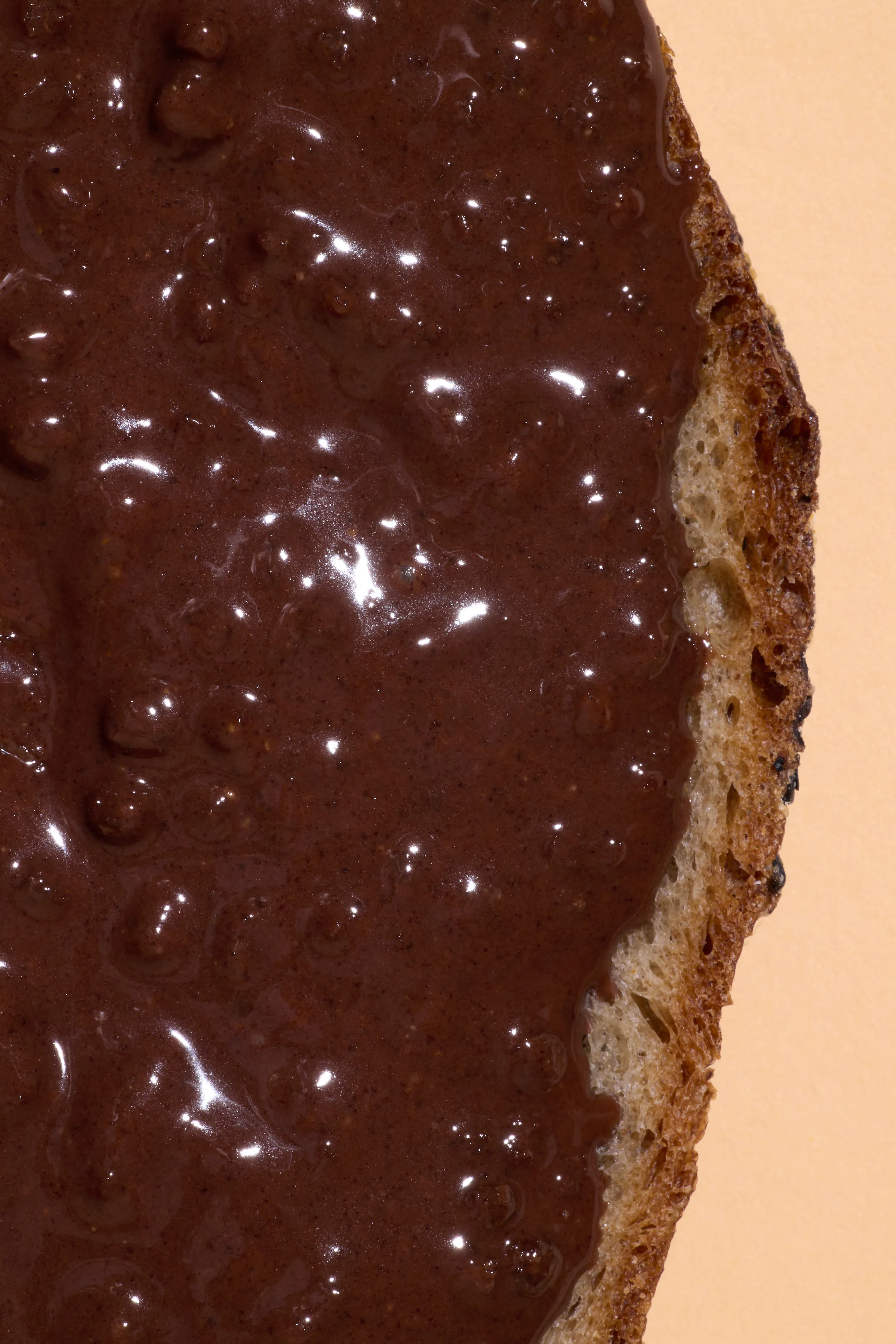 une tranche de pain recouverte d'une pâte à tartiner au chocolat brillante, avec la croûte du pain visible sur le côté droit.