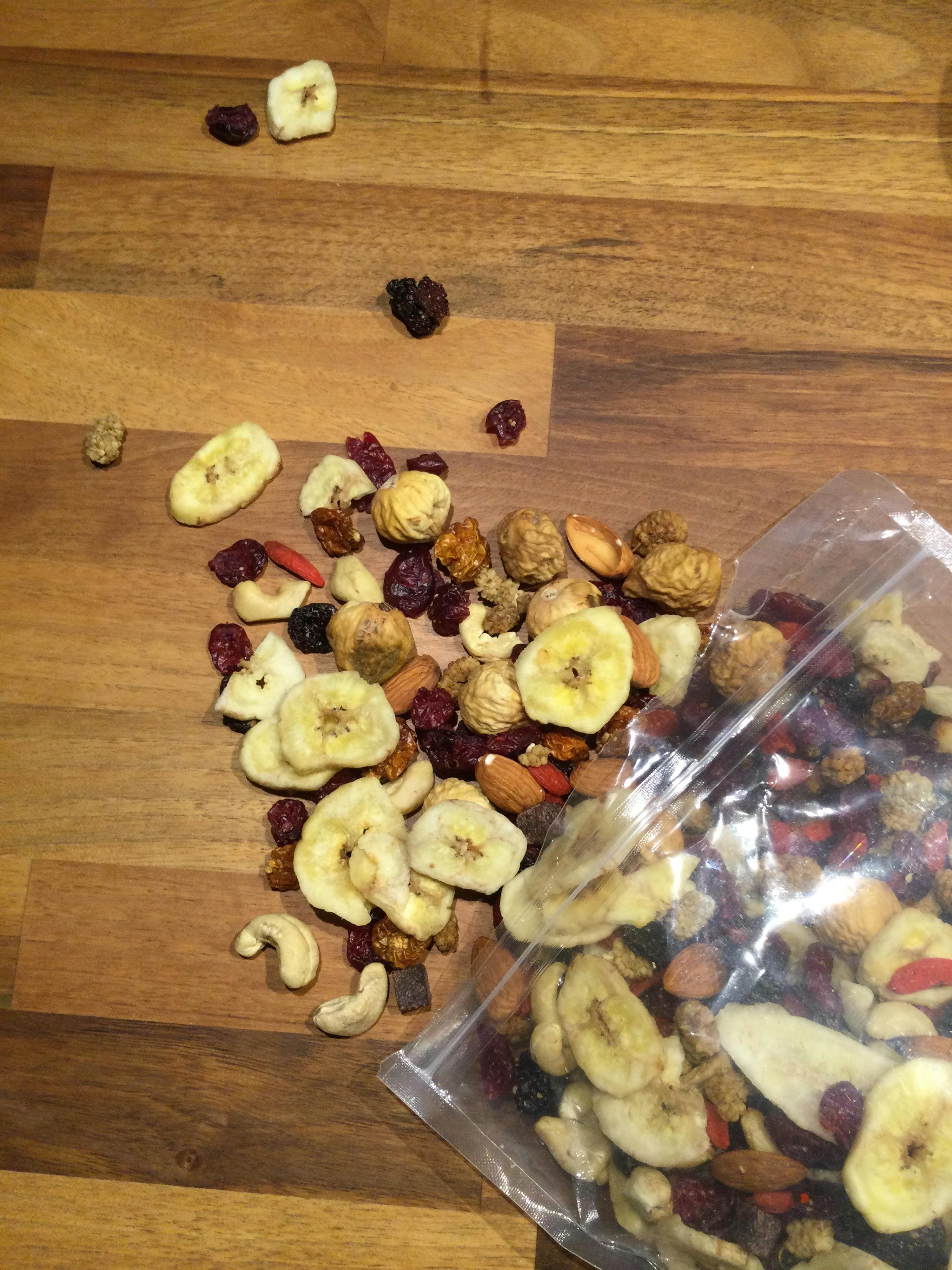eine Tüte mit getrockneten Früchten und Nüssen liegt auf einem Holztisch
