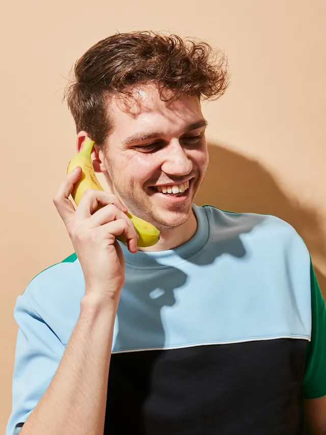 un hombre sostiene un plátano frente a su oído y sonríe