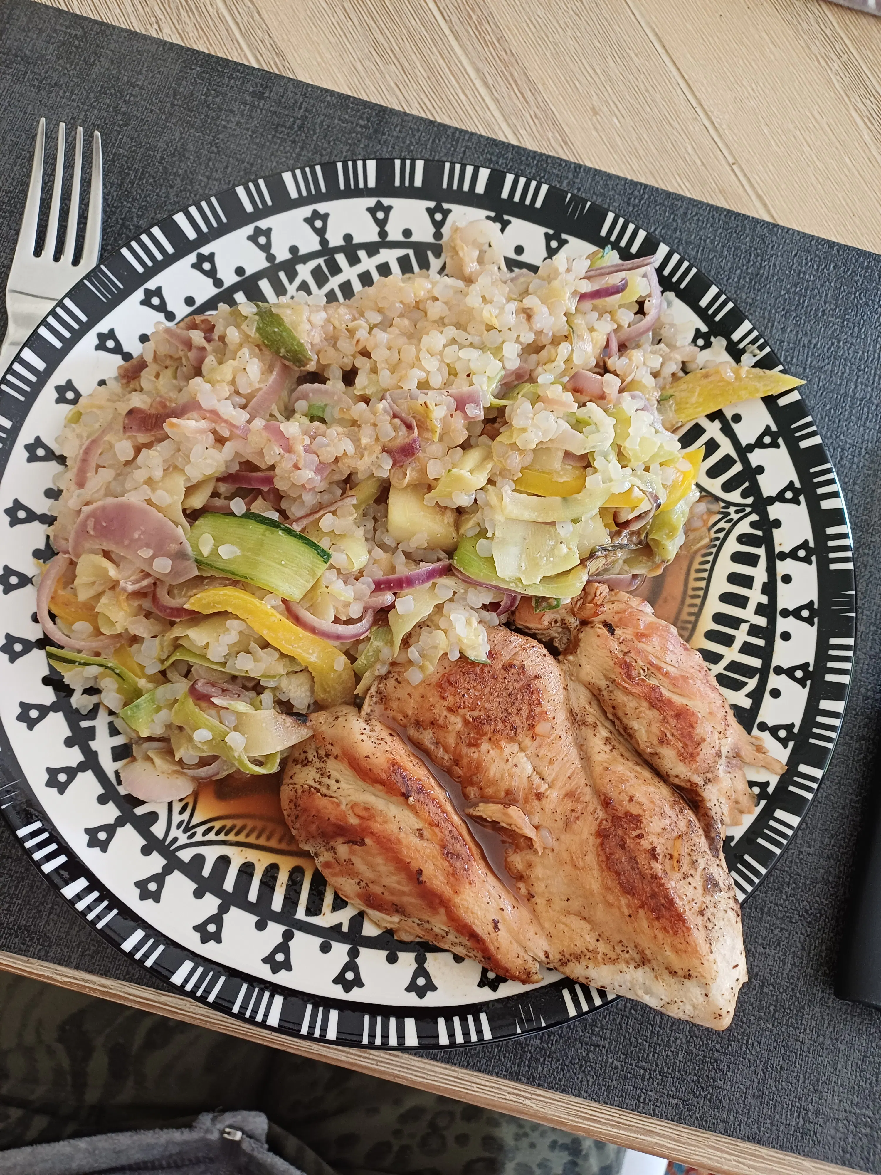 ein teller mit gebratenem hähnchenbrustfilet und einer beilage aus reis mit roten zwiebeln, gelber paprika und zucchini.