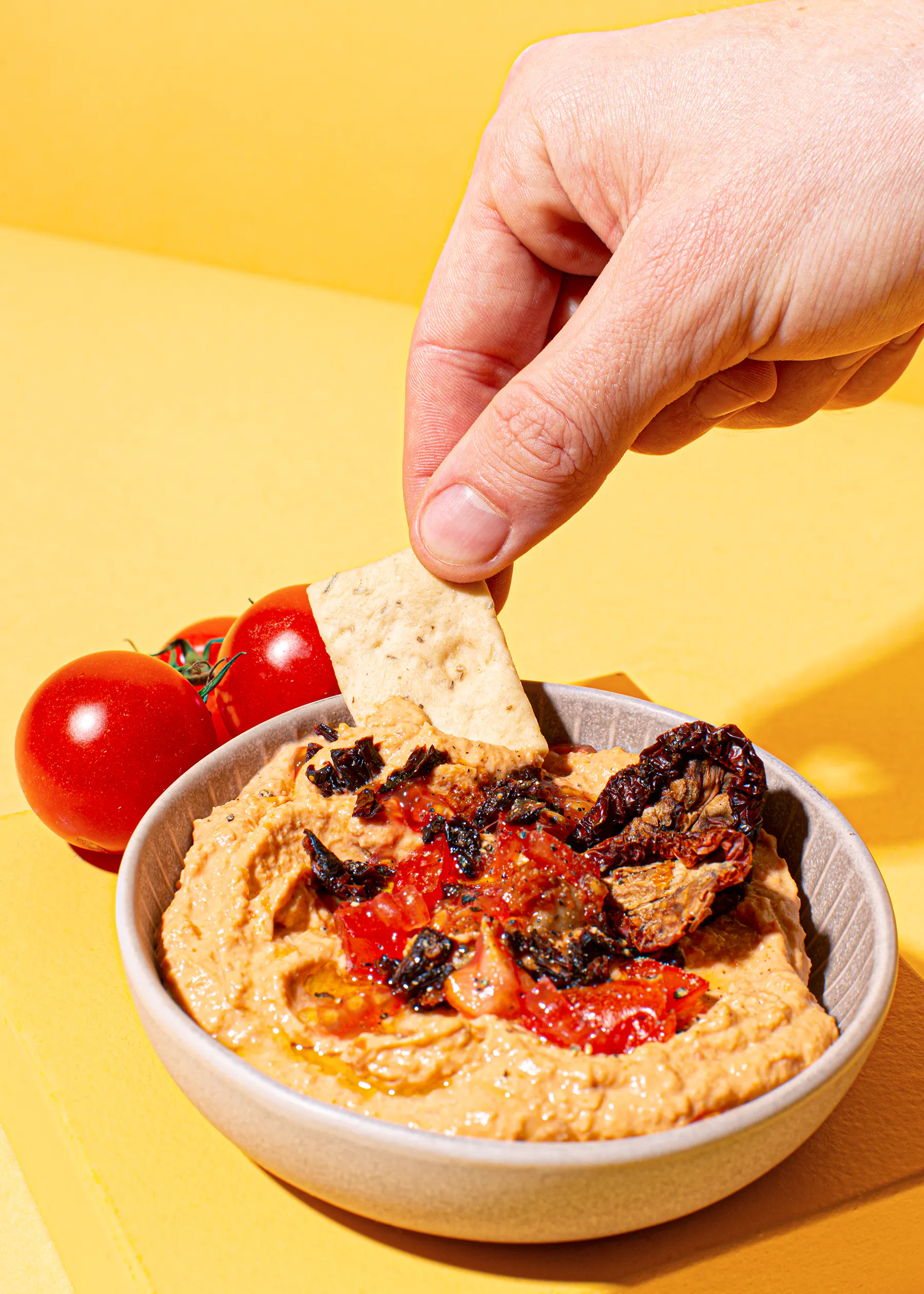 a hand dipping a cracker into a bowl of hummus