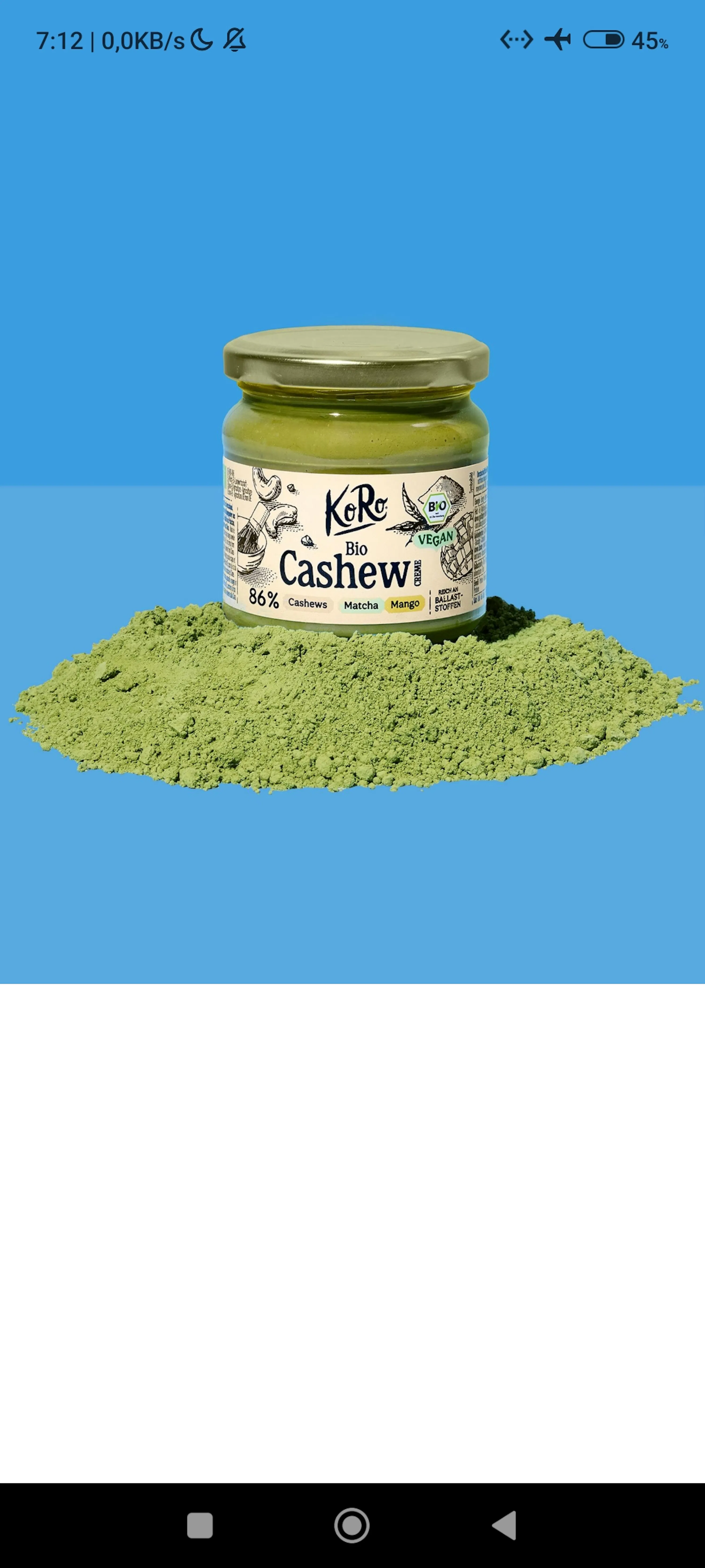 ein glas koro bio cashew creme mit matcha und mango steht auf einem haufen grünem matchapulver vor blauem hintergrund.