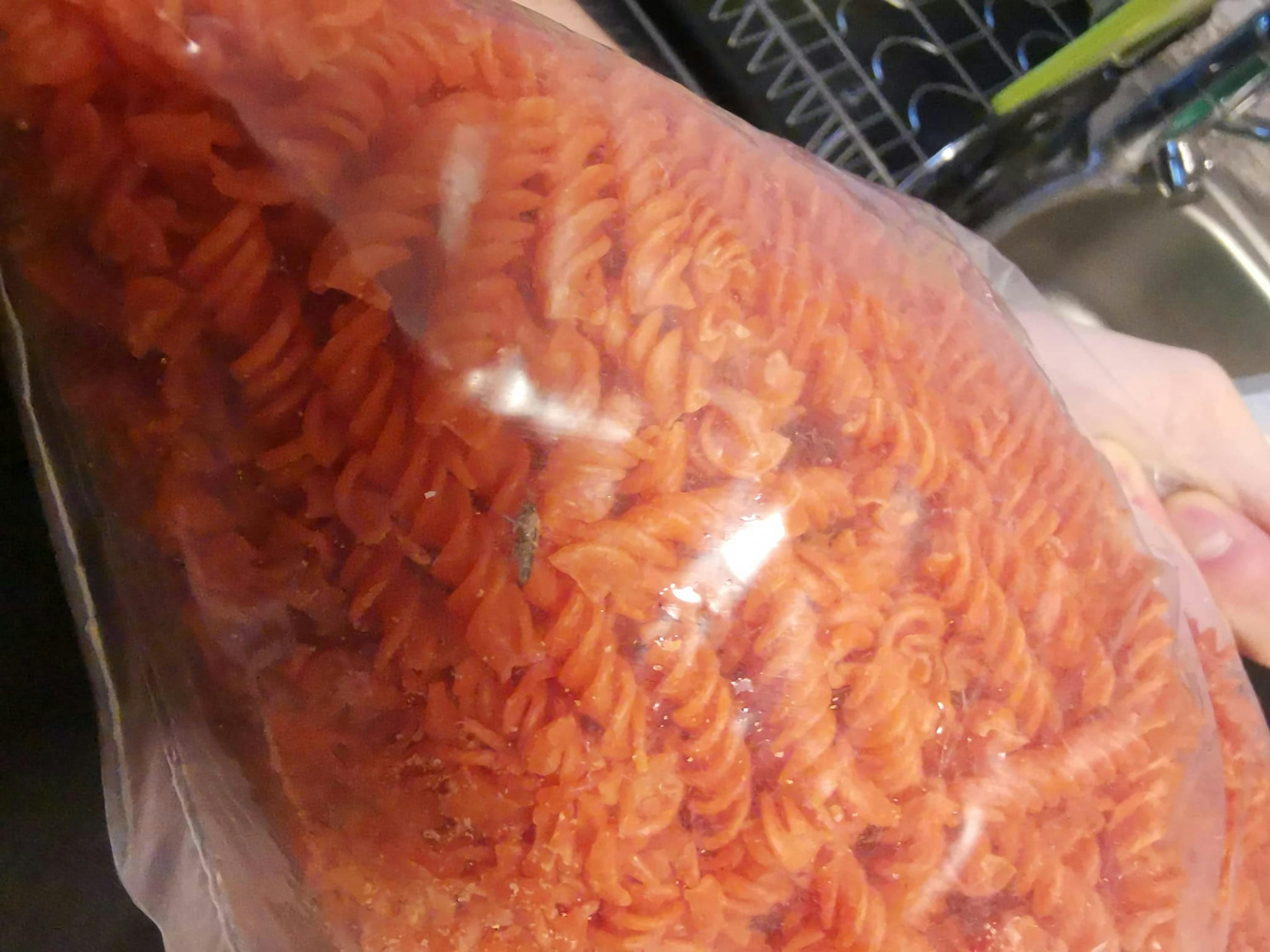 une personne tient un sac de pâtes spirales rouges