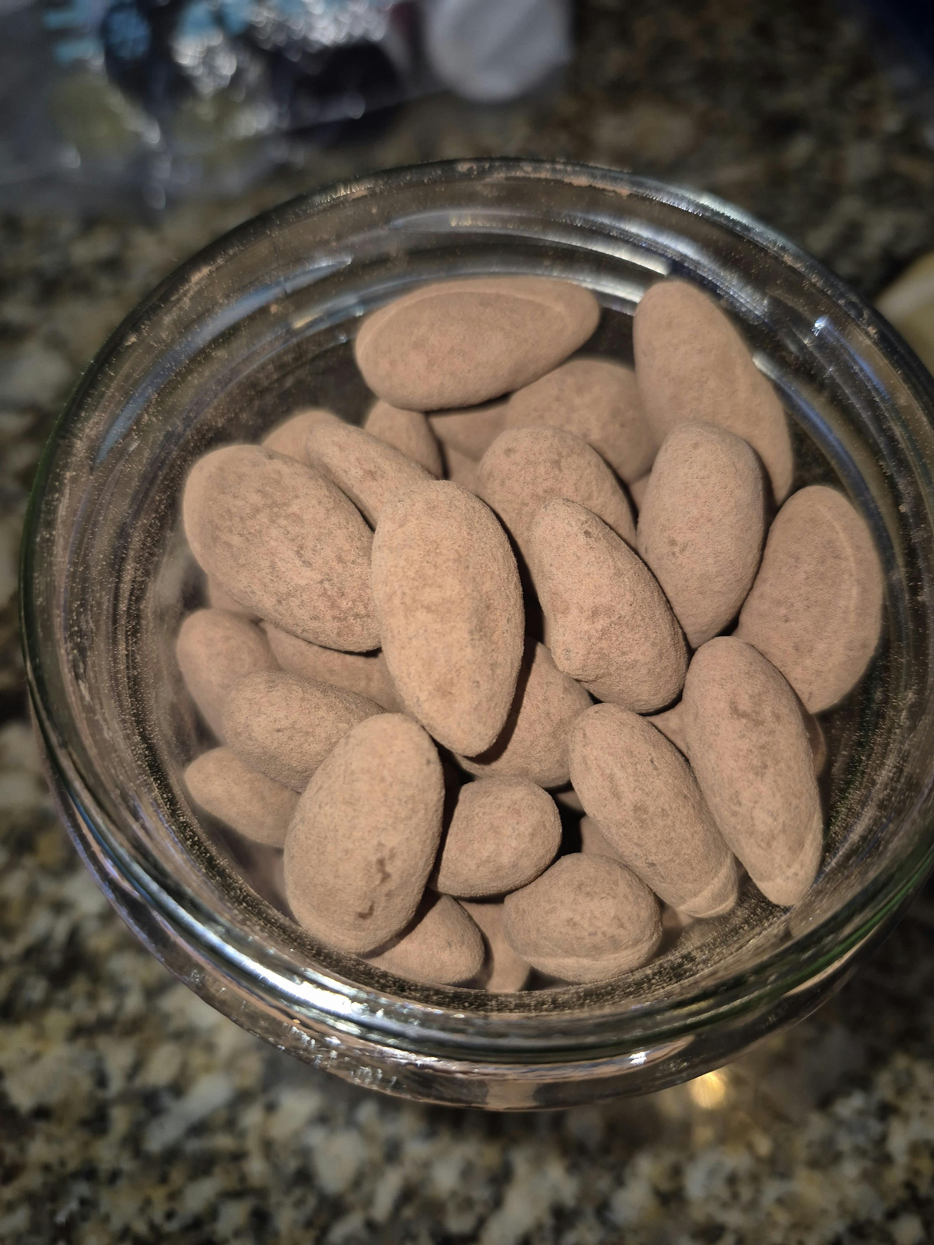 a top-down view of cocoa-dusted almonds in a clear glass jar.