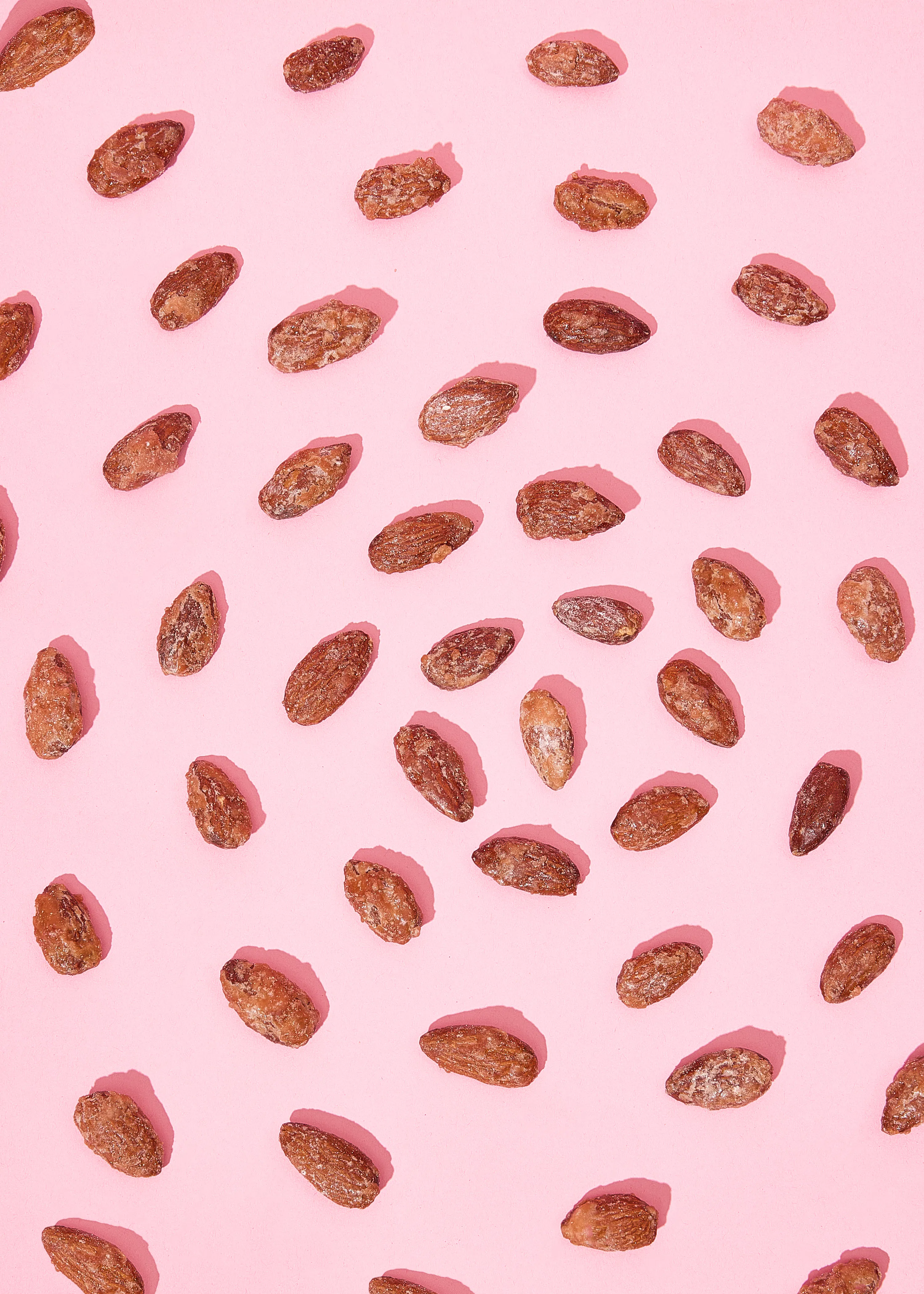 des amandes grillées sont dispersées sur un fond rose avec des ombres projetées.