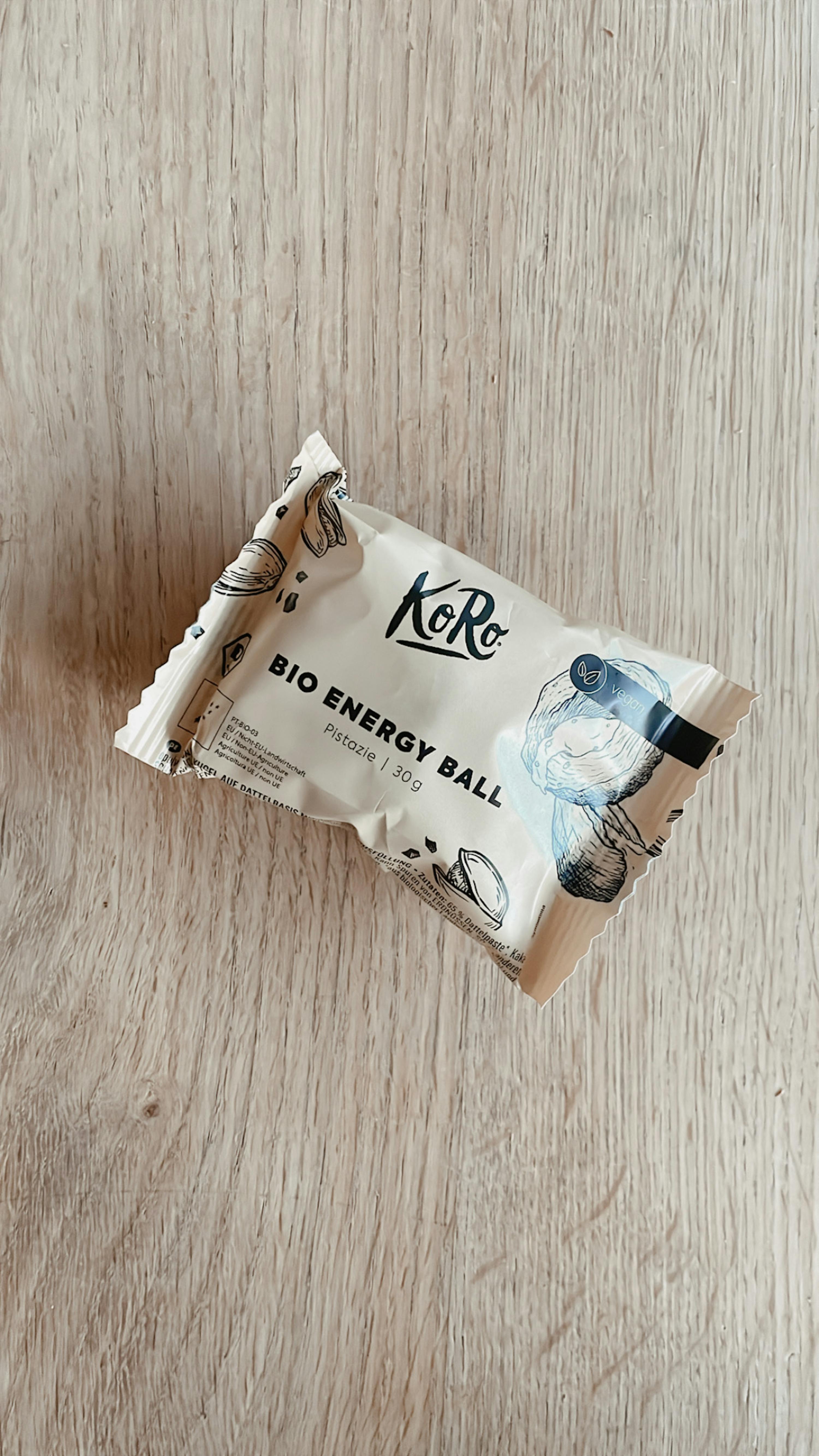 Eine verpackte Bio-Energiekugel liegt auf einem Holztisch
