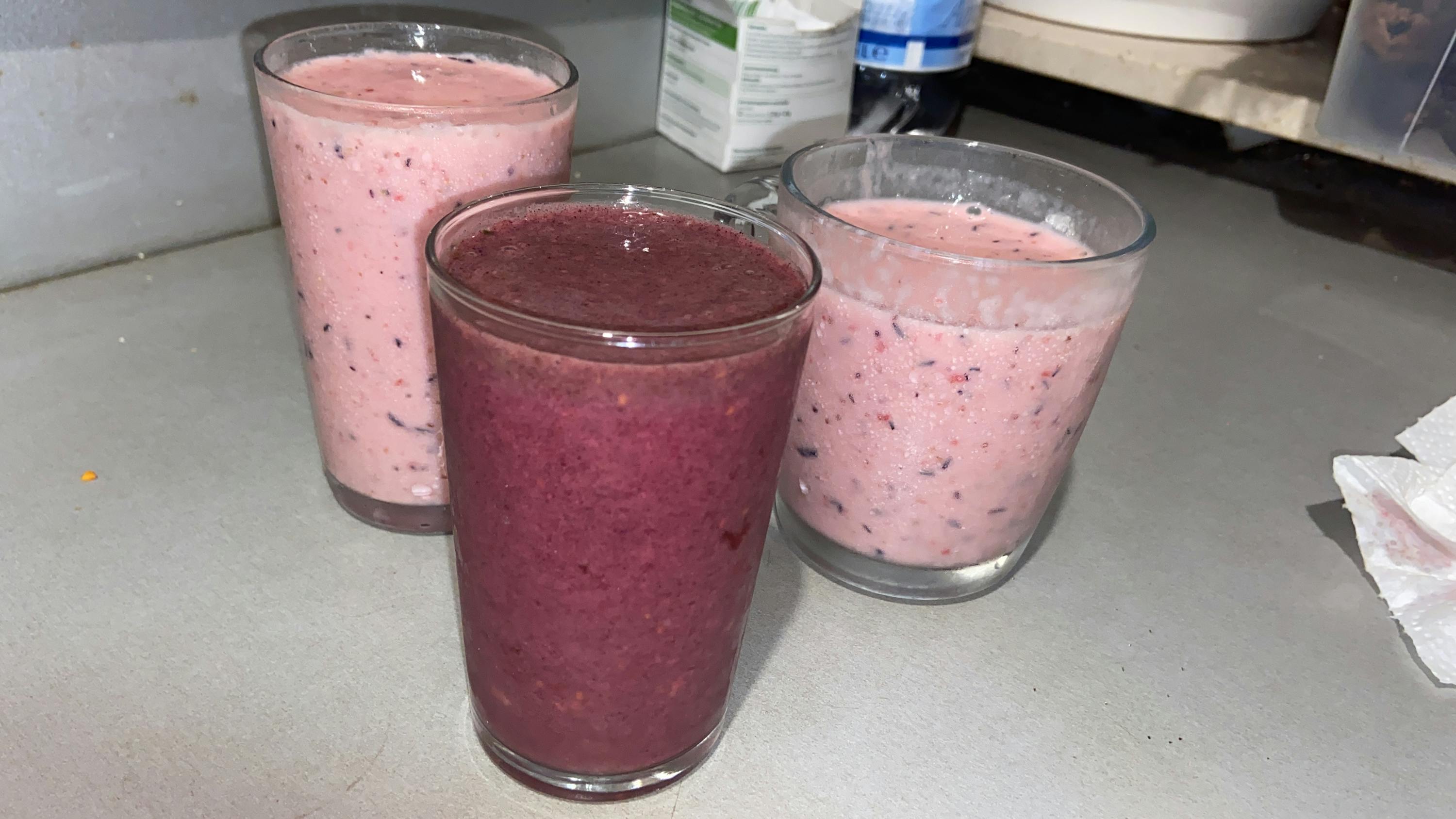drei Gläser mit verschiedenen Smoothies stehen auf einem Tisch