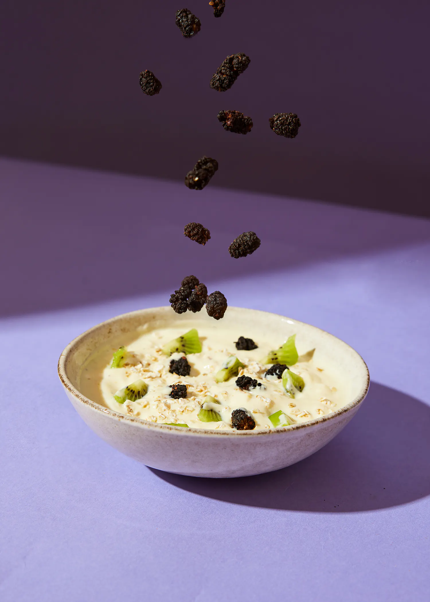 a bowl of food with blackberries and kiwi slices falling into it