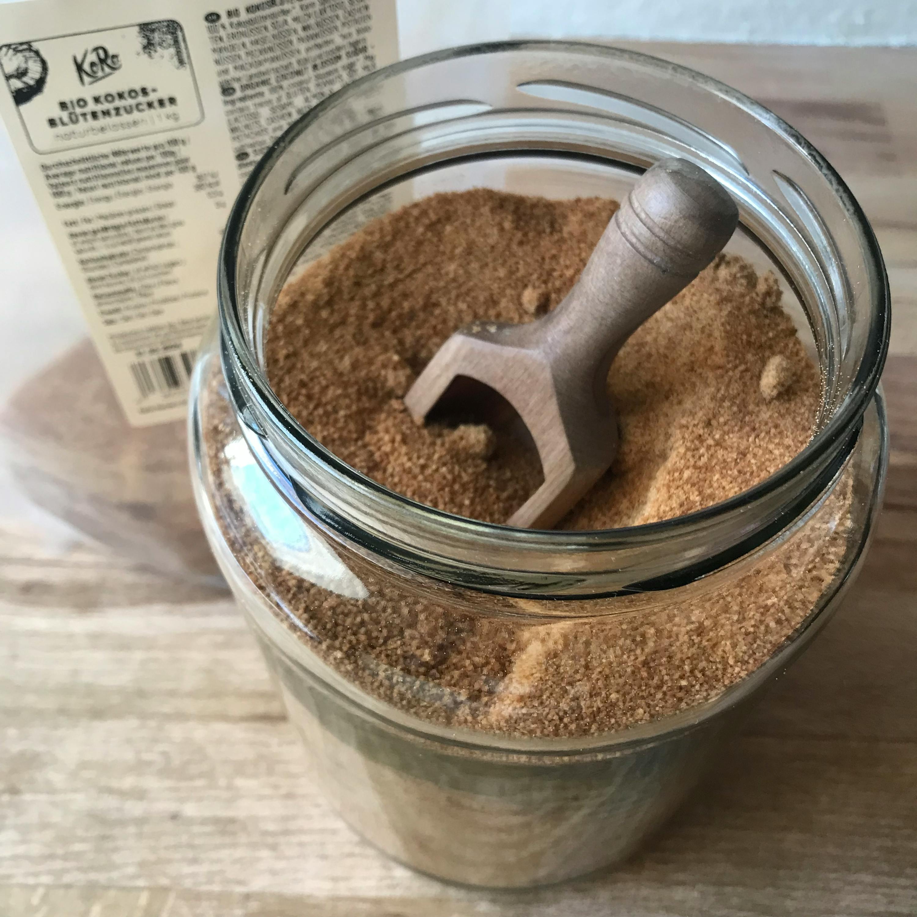 un barattolo di vetro pieno di farina di cocco e una spatola di legno