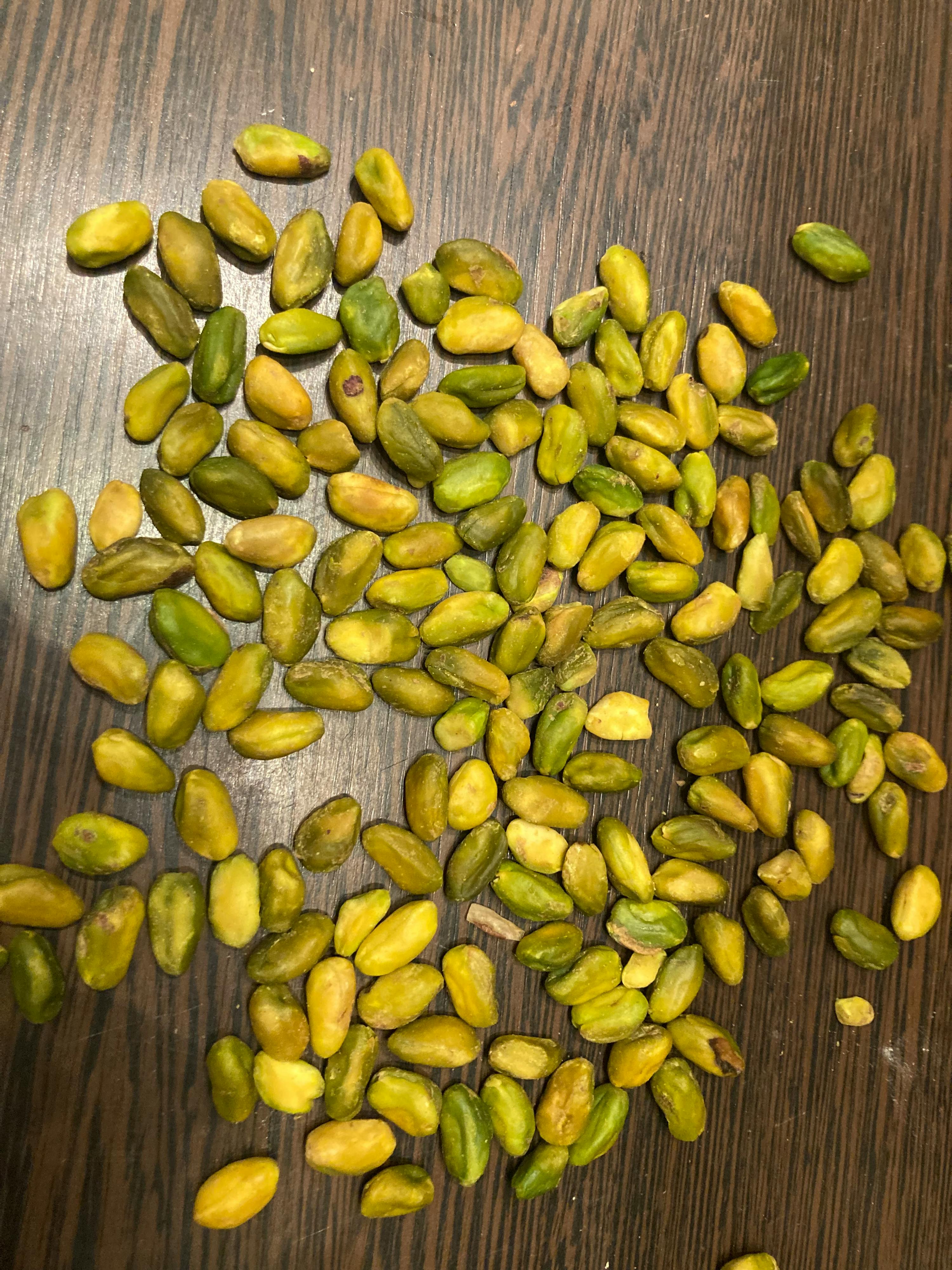 viele geschälte pistazienkerne liegen verstreut auf einer dunklen holzoberfläche.