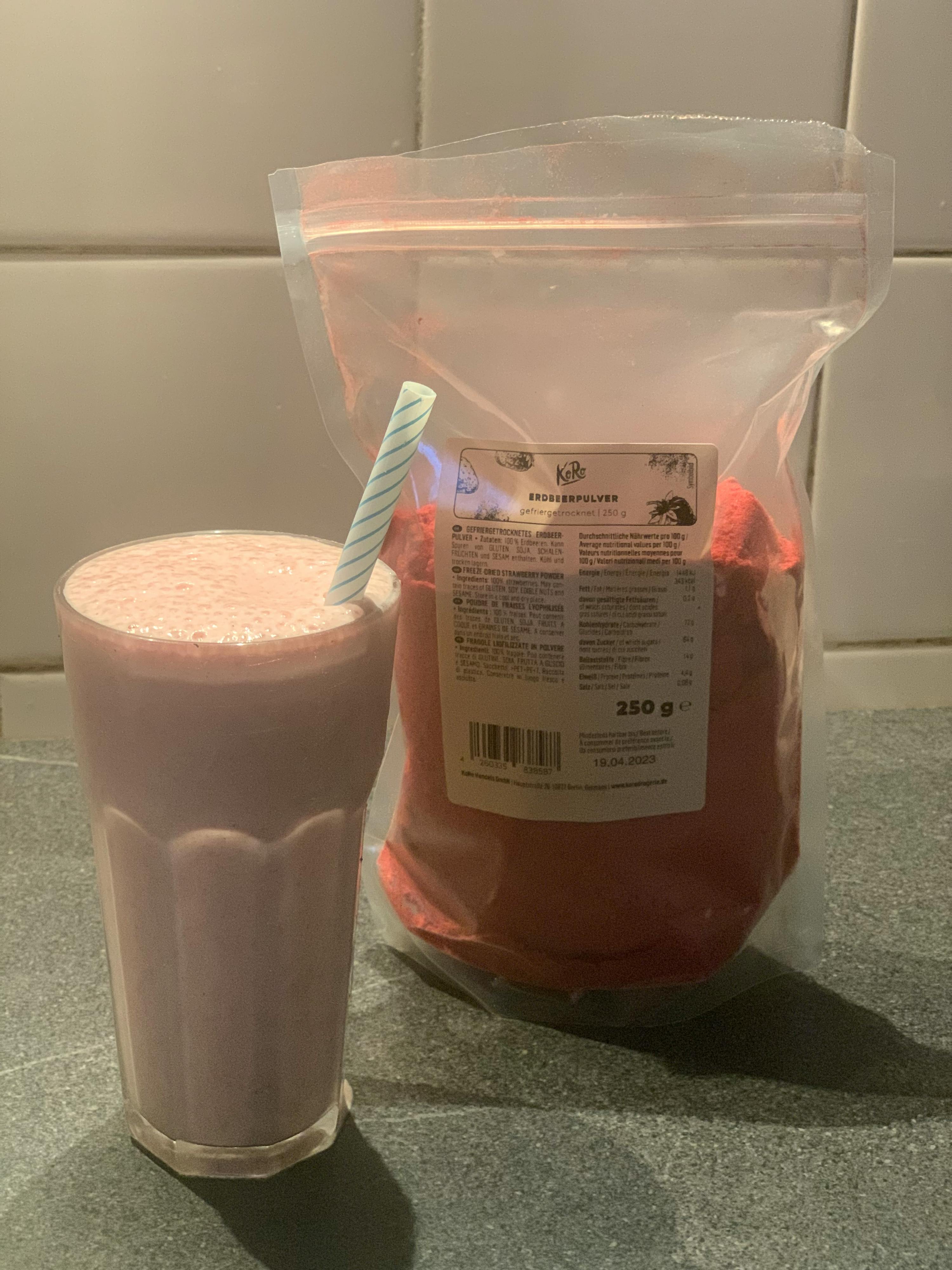 a bag of strawberry powder next to a glass of strawberry smoothie