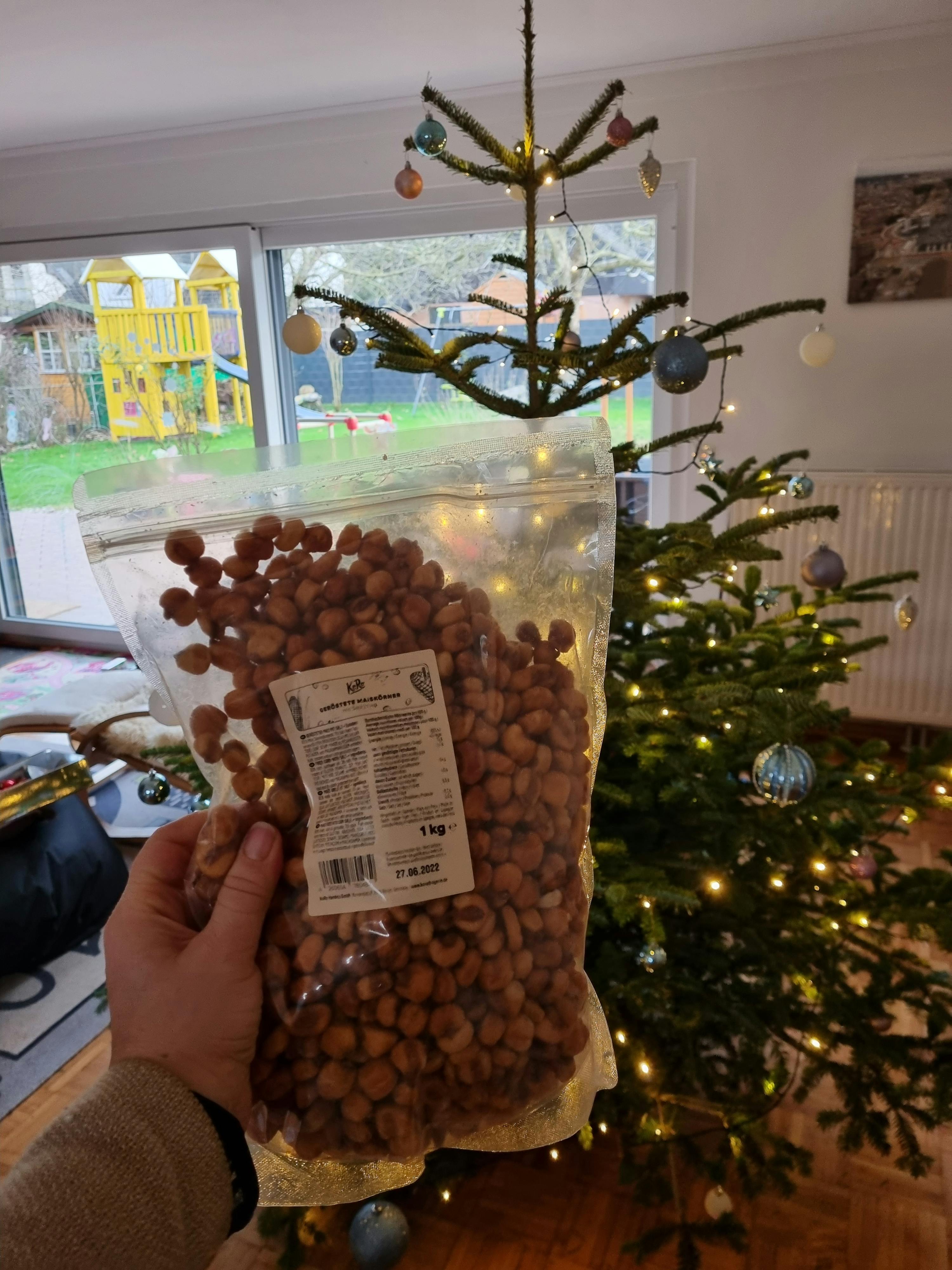 a person is holding a bag of peanuts in front of a christmas tree