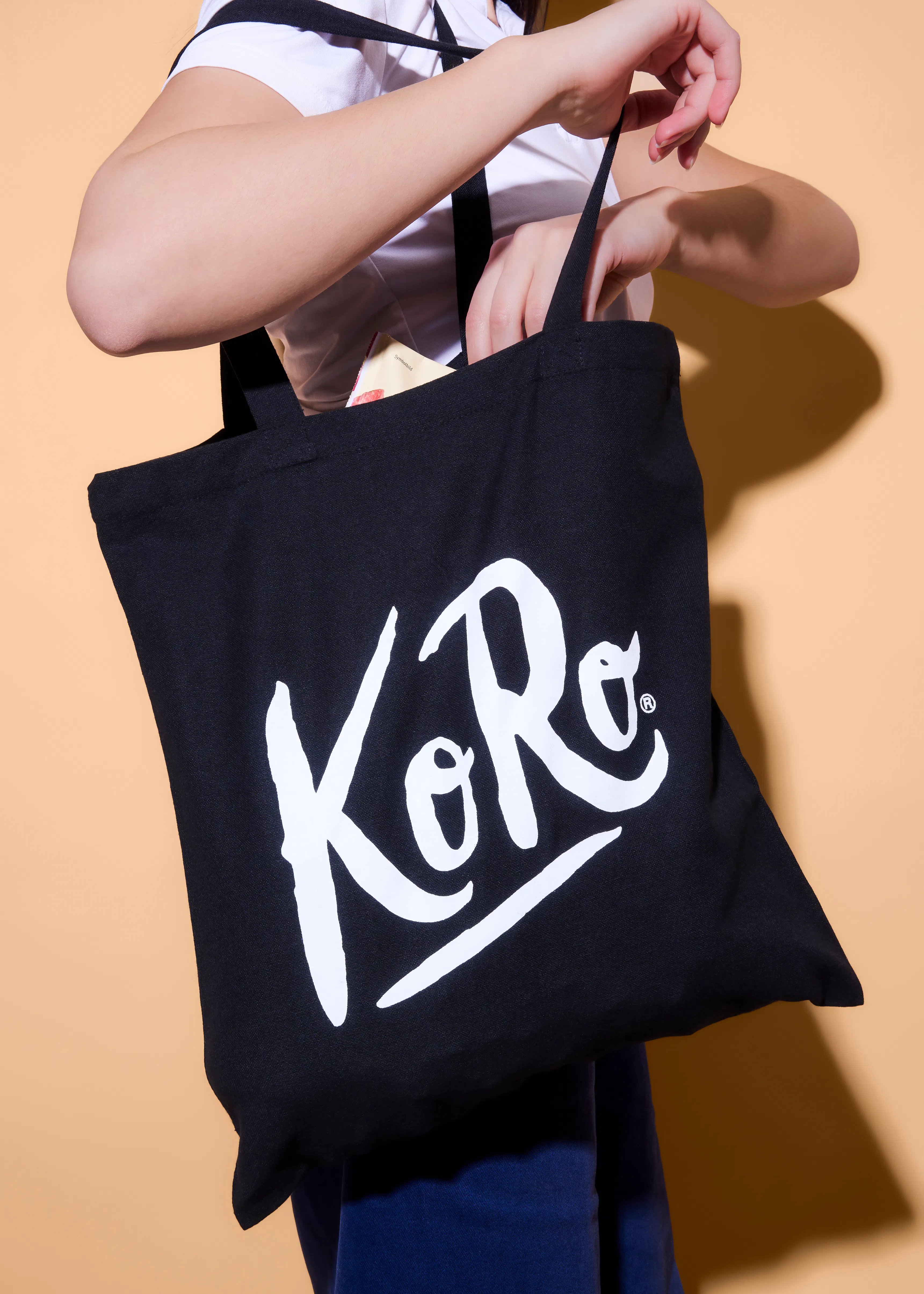 eine person steckt etwas in eine schwarze einkaufstasche mit dem weißen "koro"-logo.