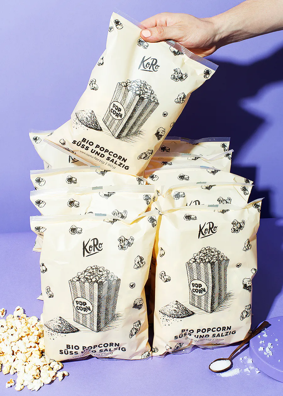 une personne tient trois sacs de pop-corn sur une table violette