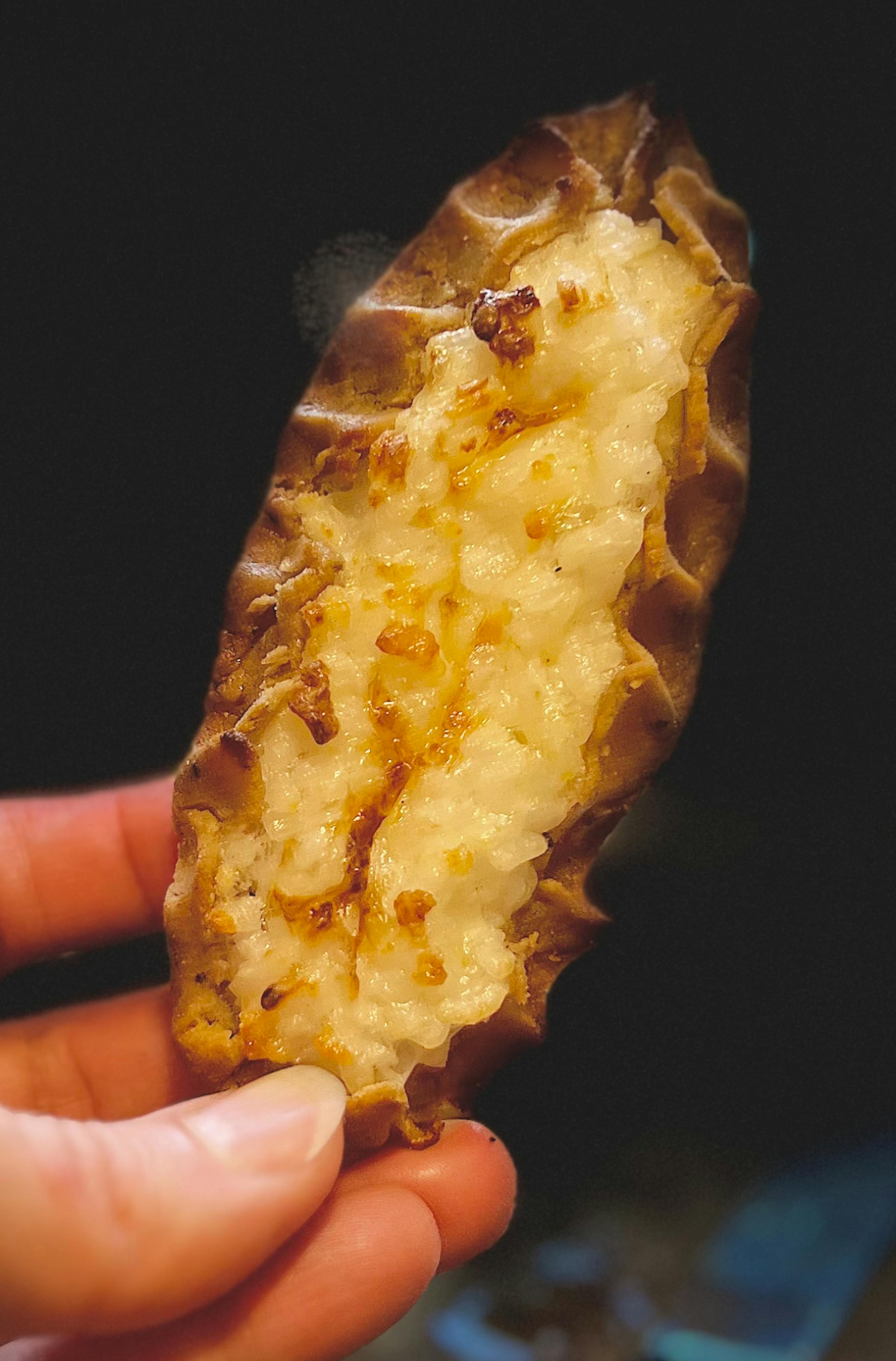 eine hand hält eine warme karjalanpiirakka, eine finnische reisbrei-pastete mit einer dunklen, geriffelten kruste und leicht gebräunter füllung.